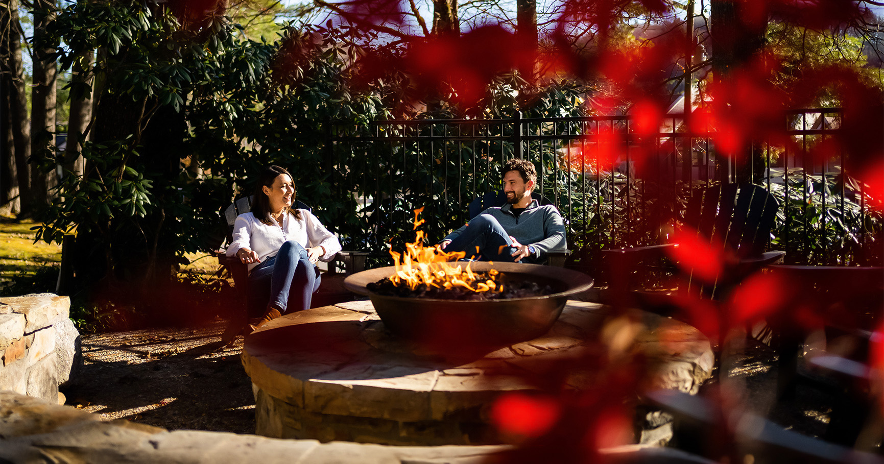 a man and woman sitting in chairs around a fire pit