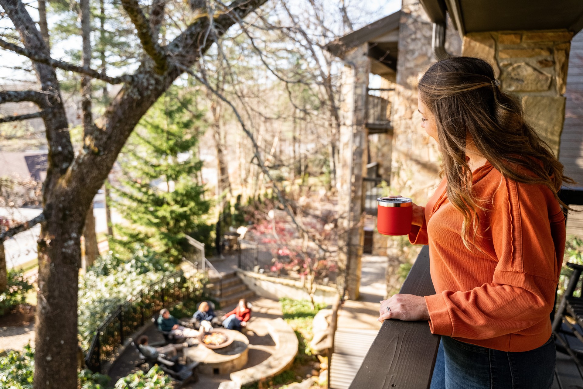 a woman standing on a balcony looking out a tree and a fire pit