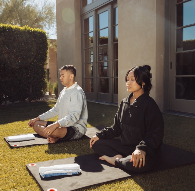 a man and woman sitting on mats outside