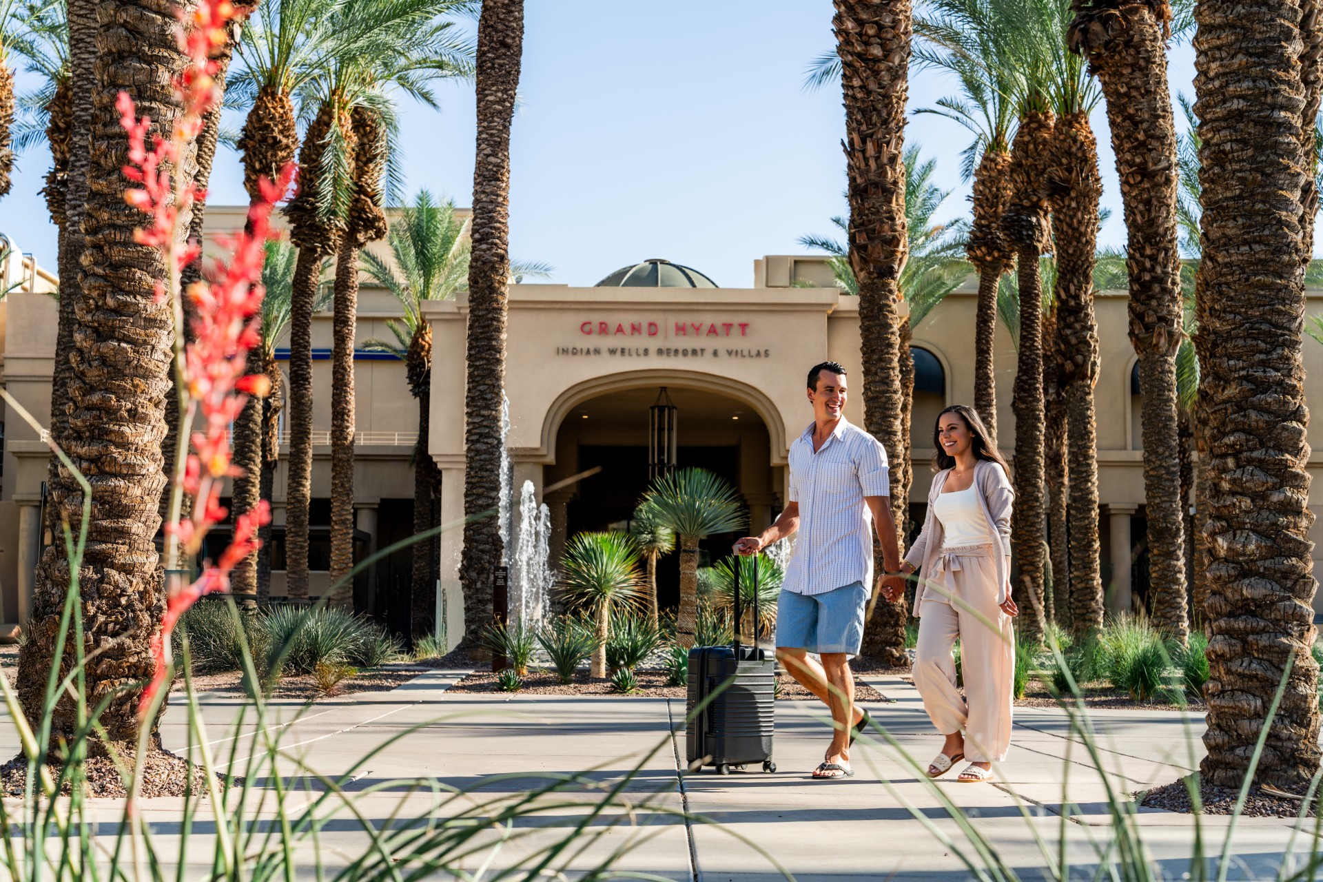 a man and woman walking with luggage in front of a building