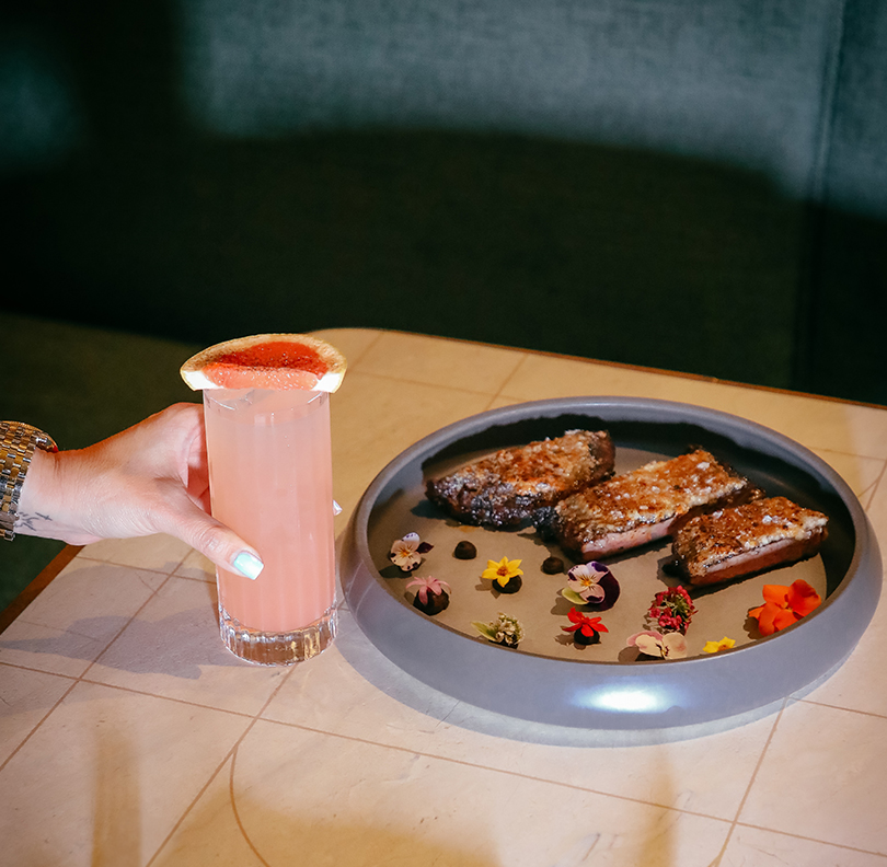 a hand holding a drink next to a plate of food
