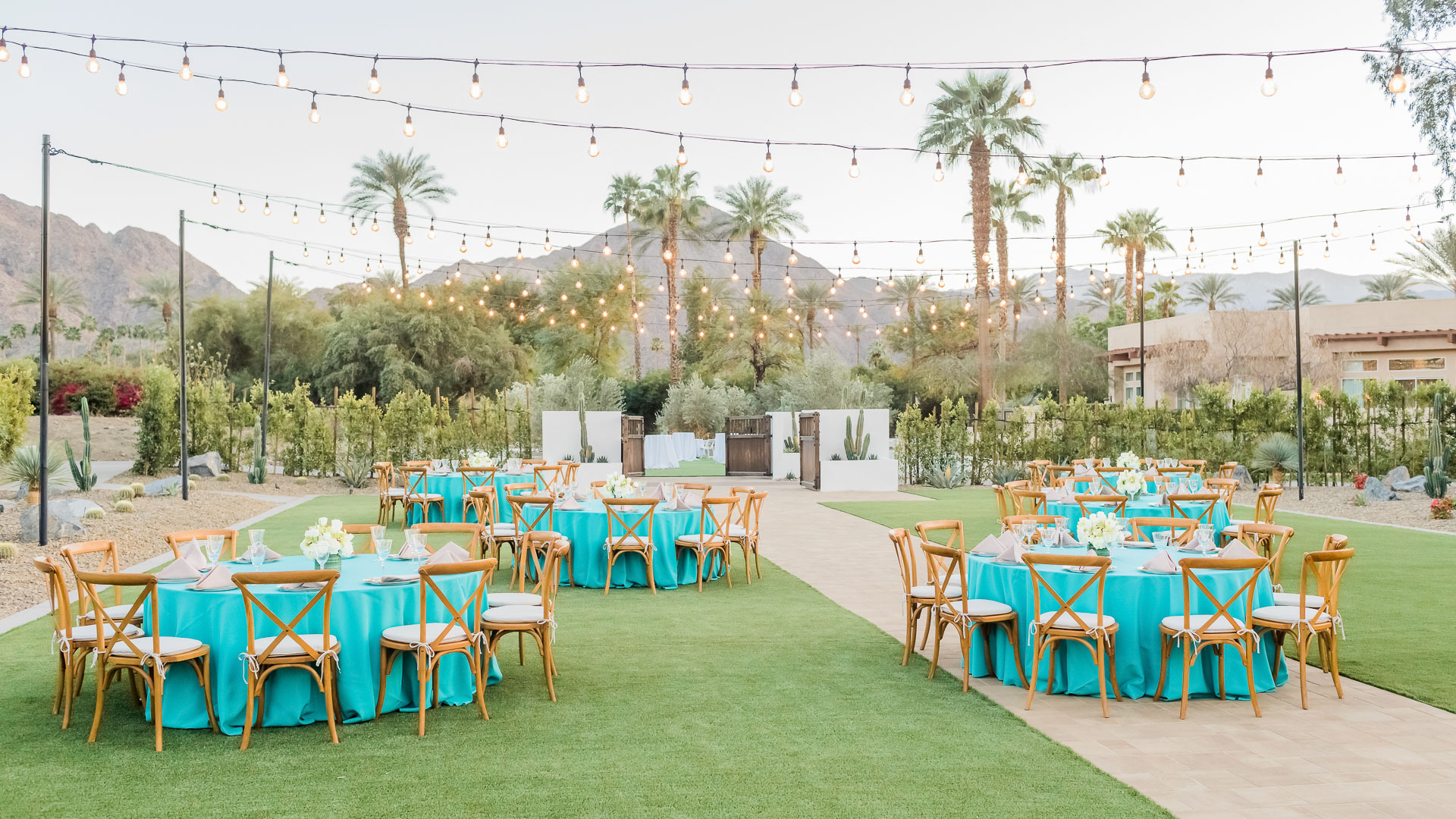 a group of tables and chairs in a yard with string lights
