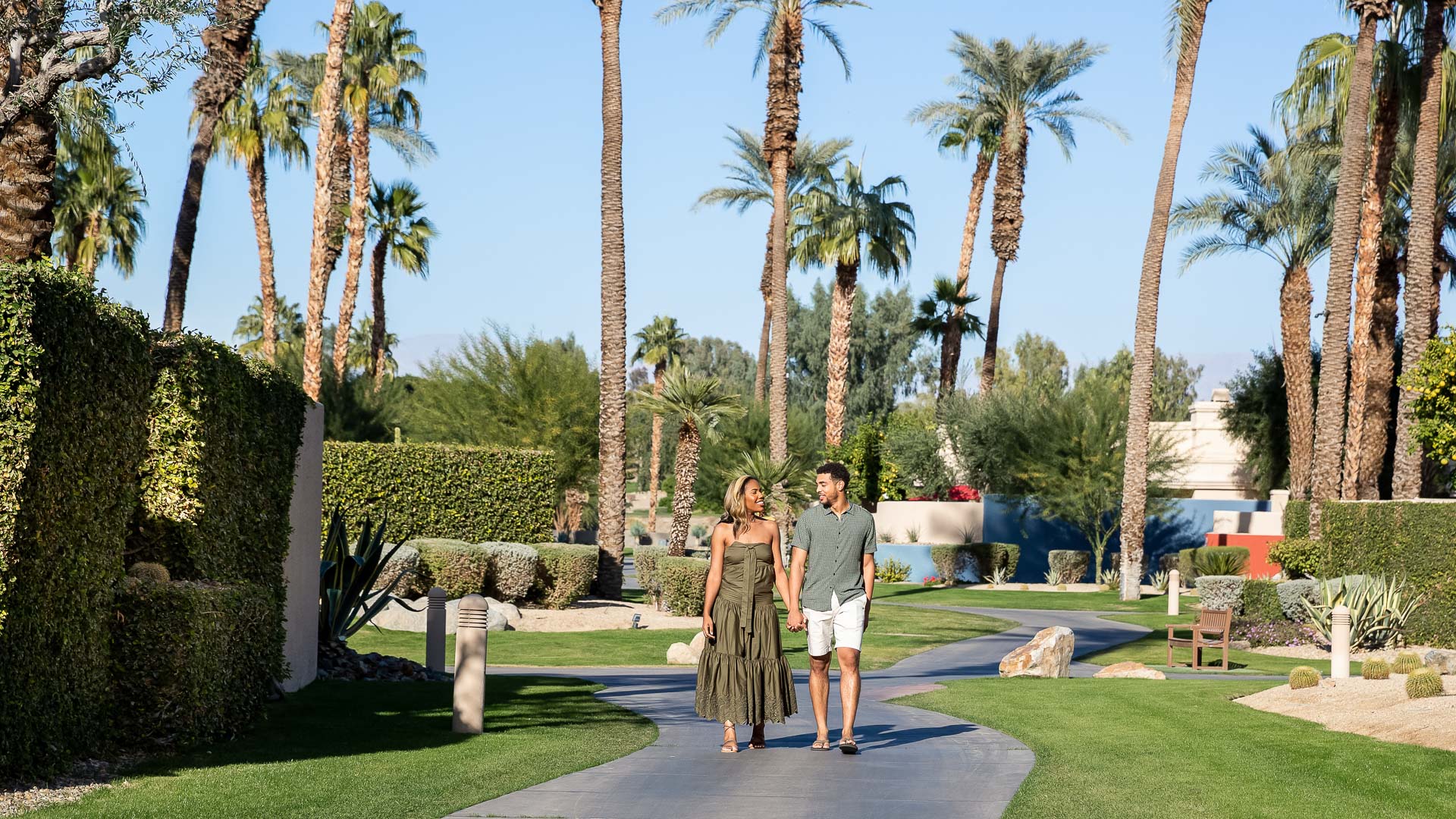 a man and woman walking on a path with palm trees