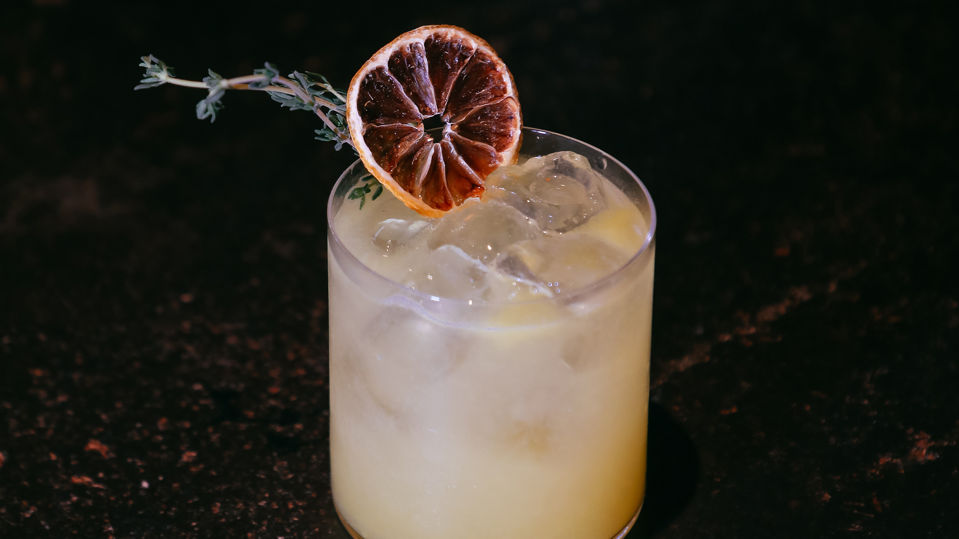 a glass of liquid with a slice of orange and a twig