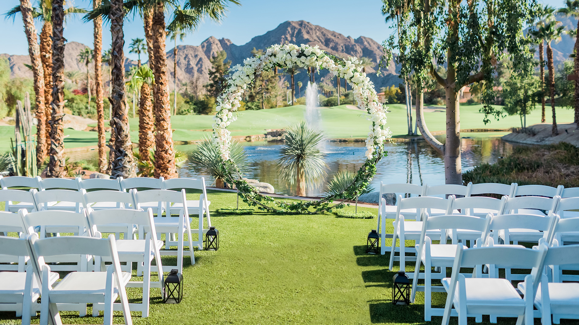 a wedding ceremony with white chairs and a fountain