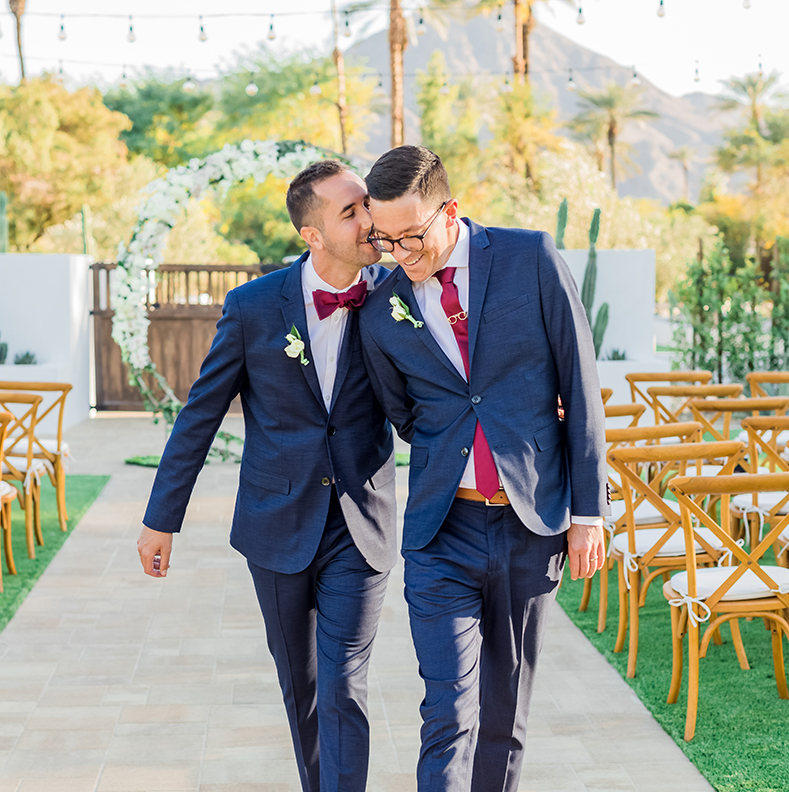 two men in suits walking down a path with chairs and trees