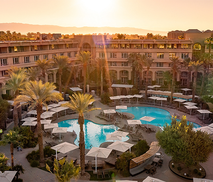 a pool with umbrellas and palm trees in front of a building