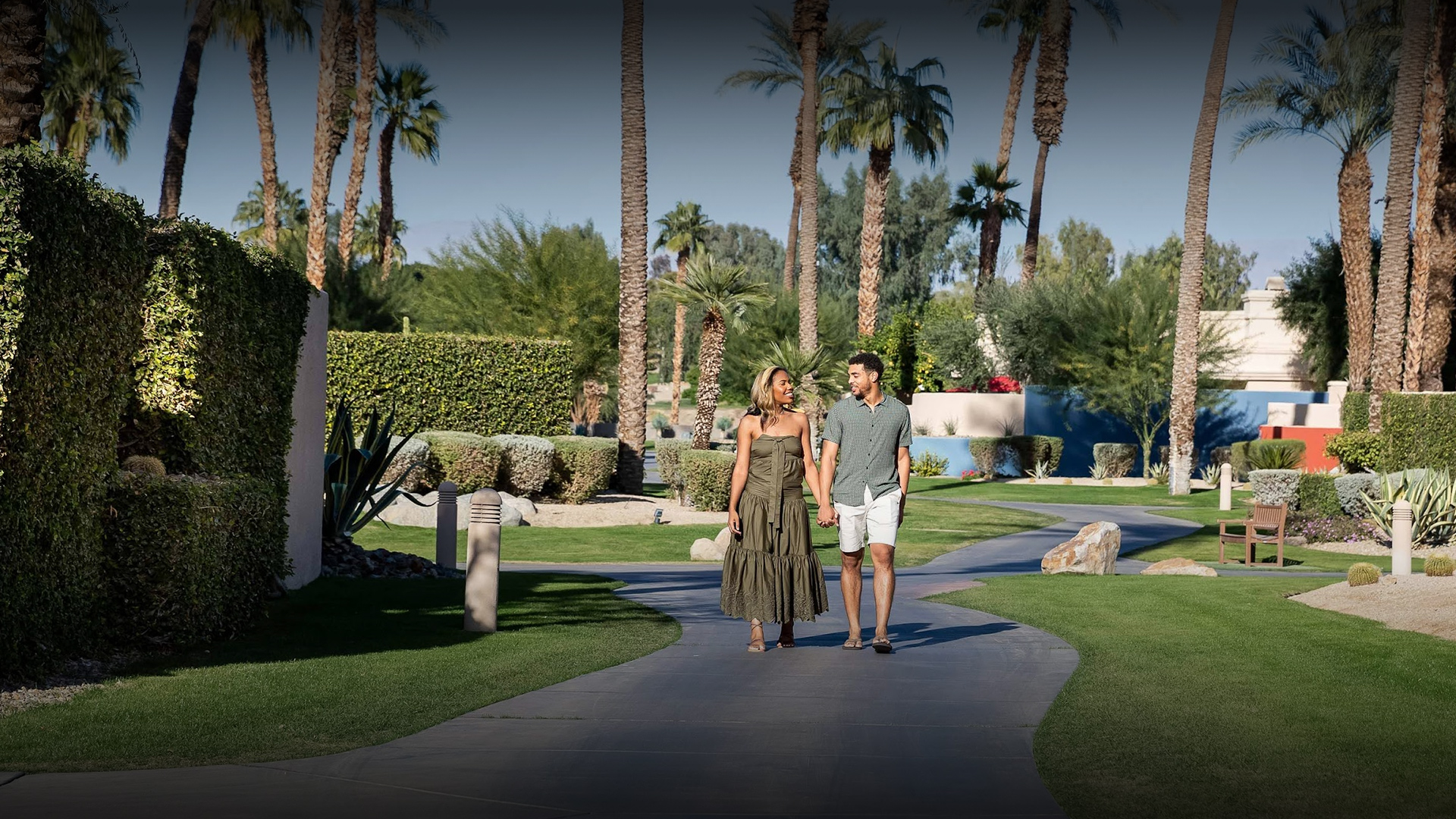 a man and woman holding hands walking down a path