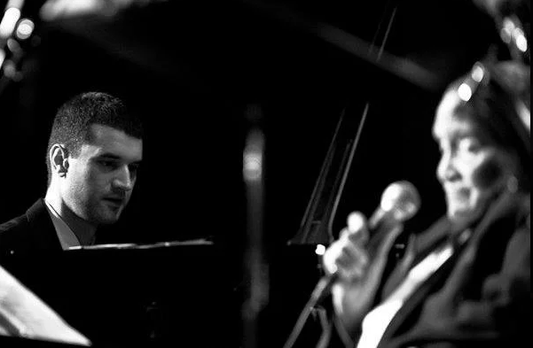 a man holding a microphone next to a man playing a cello