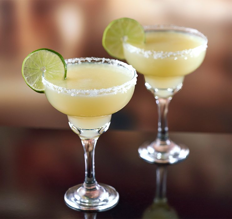 two glasses of yellow liquid with lime slices on top