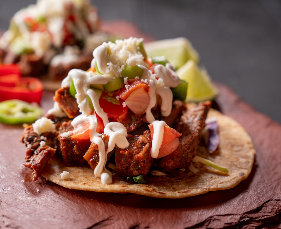 a taco with meat and vegetables on a stone surface