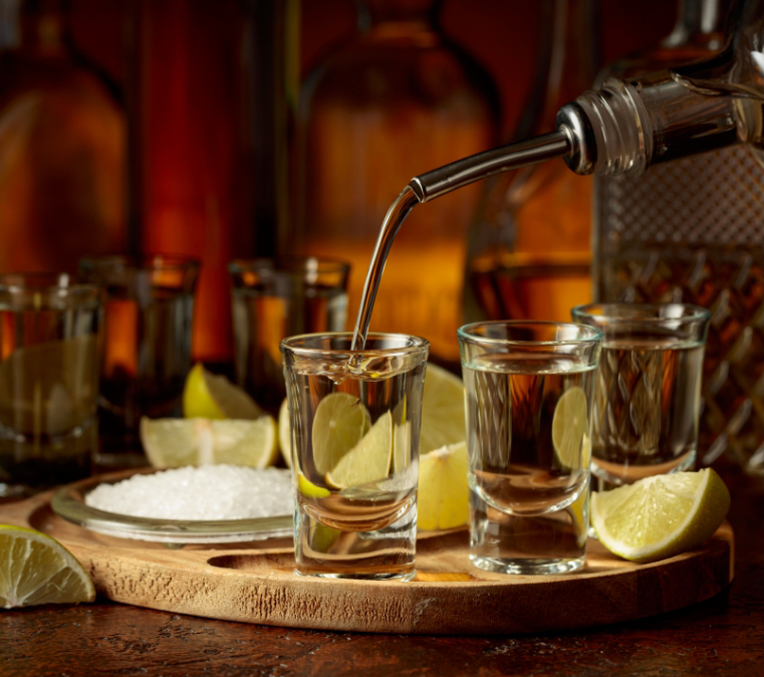 a group of shot glasses with limes and a silver metal bottle being poured into them