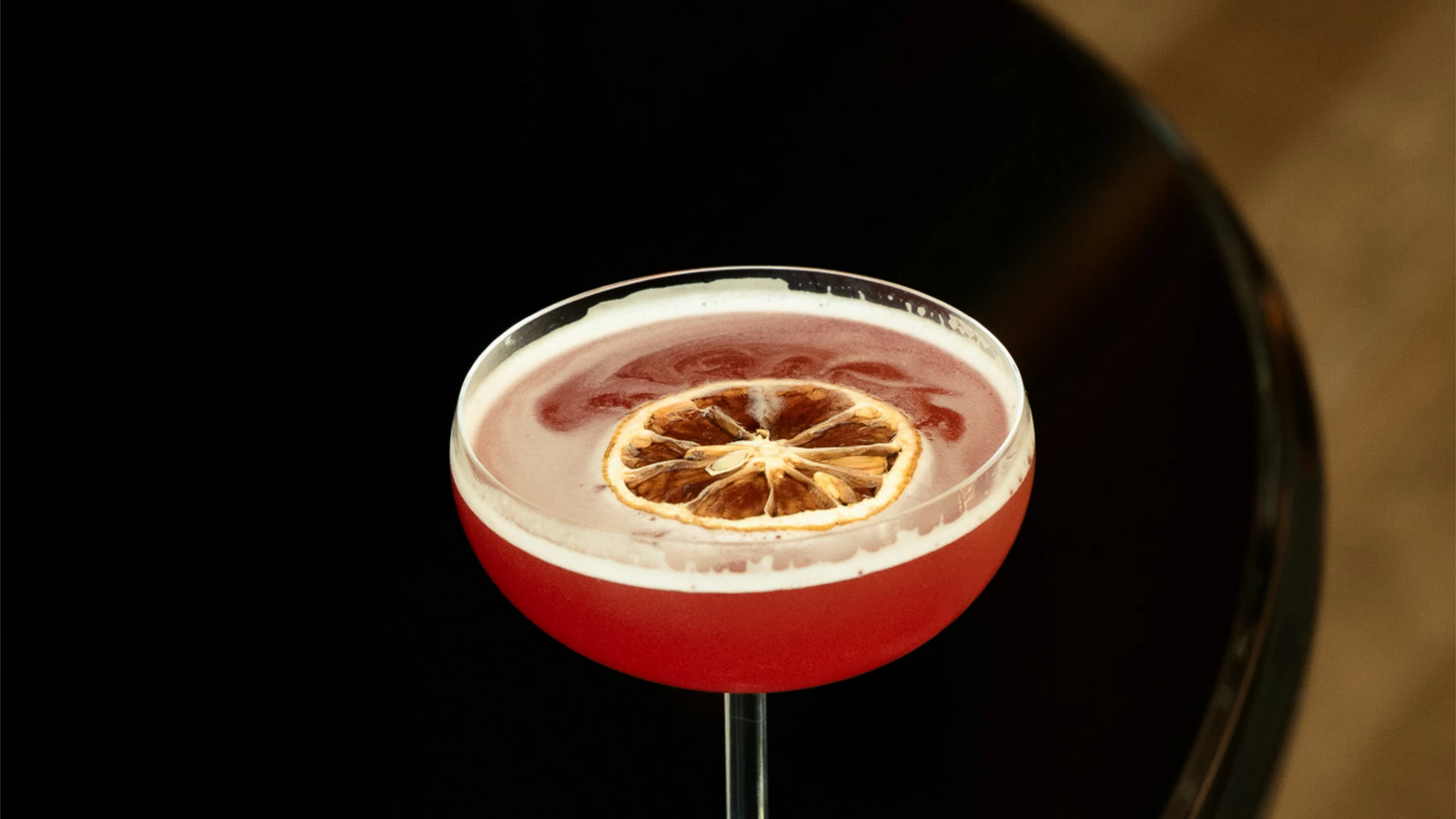 a red cocktail in a stemmed glass with a lemon slice