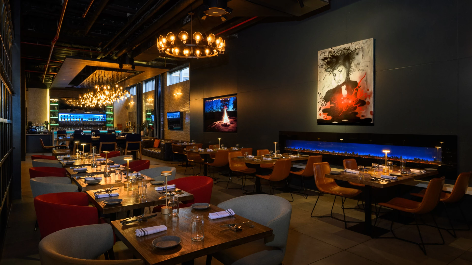 a dimly lit dining area with tables set for dinner, chairs, lighting fixtures, artwork on the walls, and a fireplace
