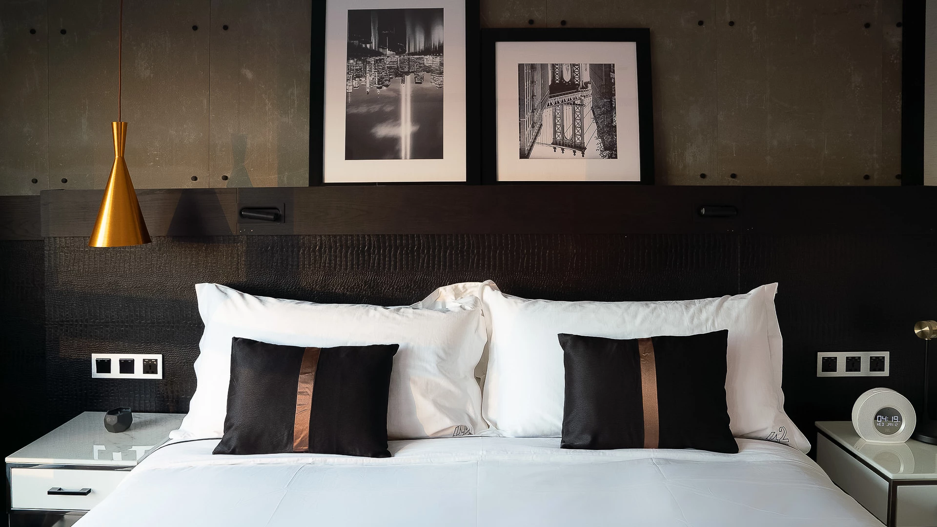 A neatly made bed with white and black pillows and a dark headboard