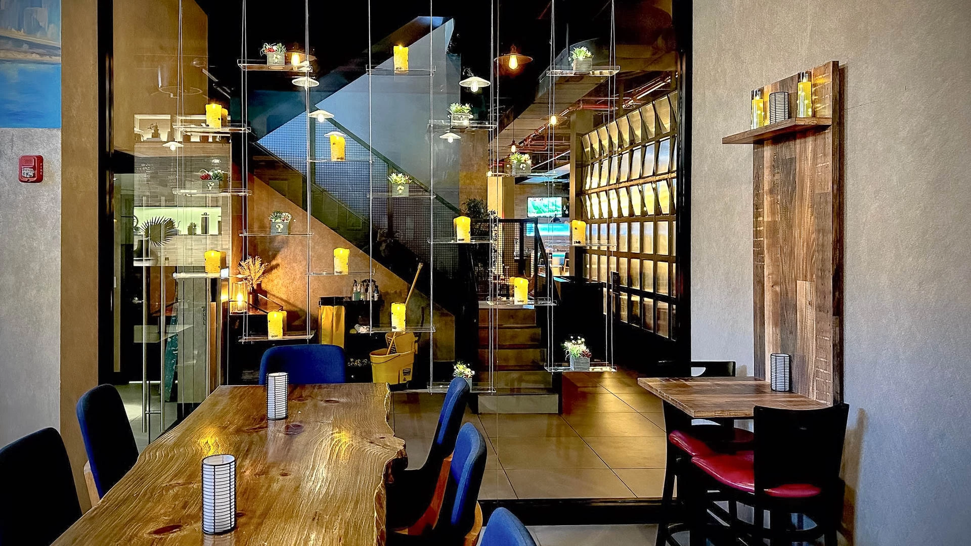 A dining area with a wooden table and chairs, candle lights, and a glass partition.