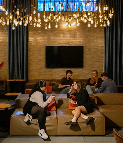 A lounge area with people sitting on leather couches, a coffee table, and a large chandelier hanging from the ceiling.