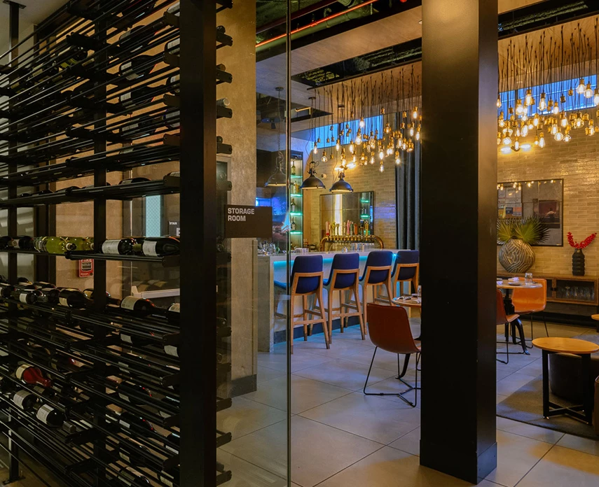 A dimly lit bar area with a large wine rack, a bar counter with stools, and a chandelier hanging from the ceiling.