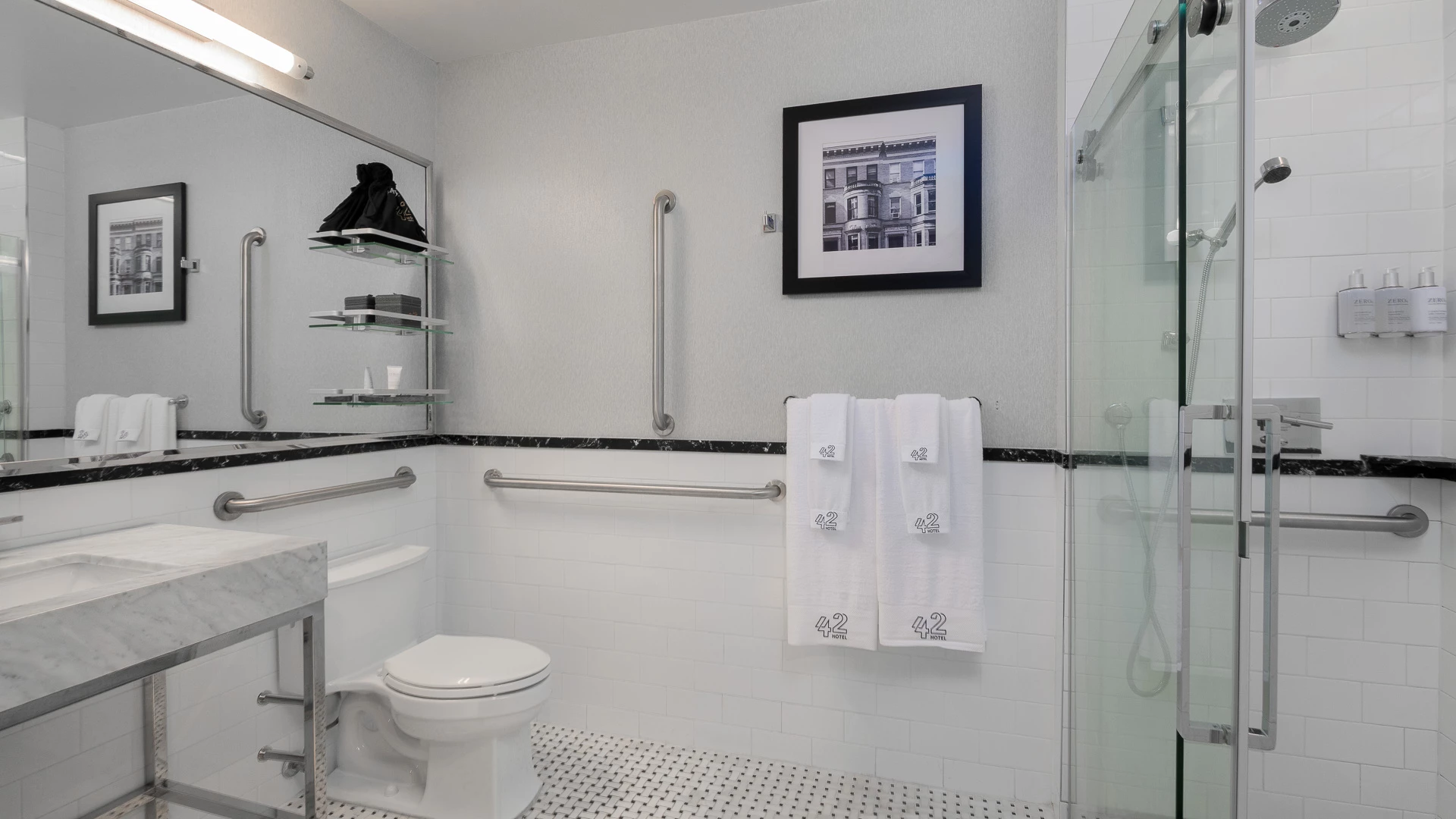 A clean and modern bathroom with white tiles, a glass-enclosed shower, and grab bars.