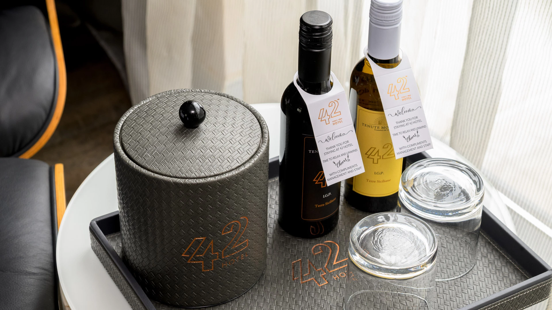 A hotel room amenity with wine bottles, glasses, and an ice bucket on a tray.