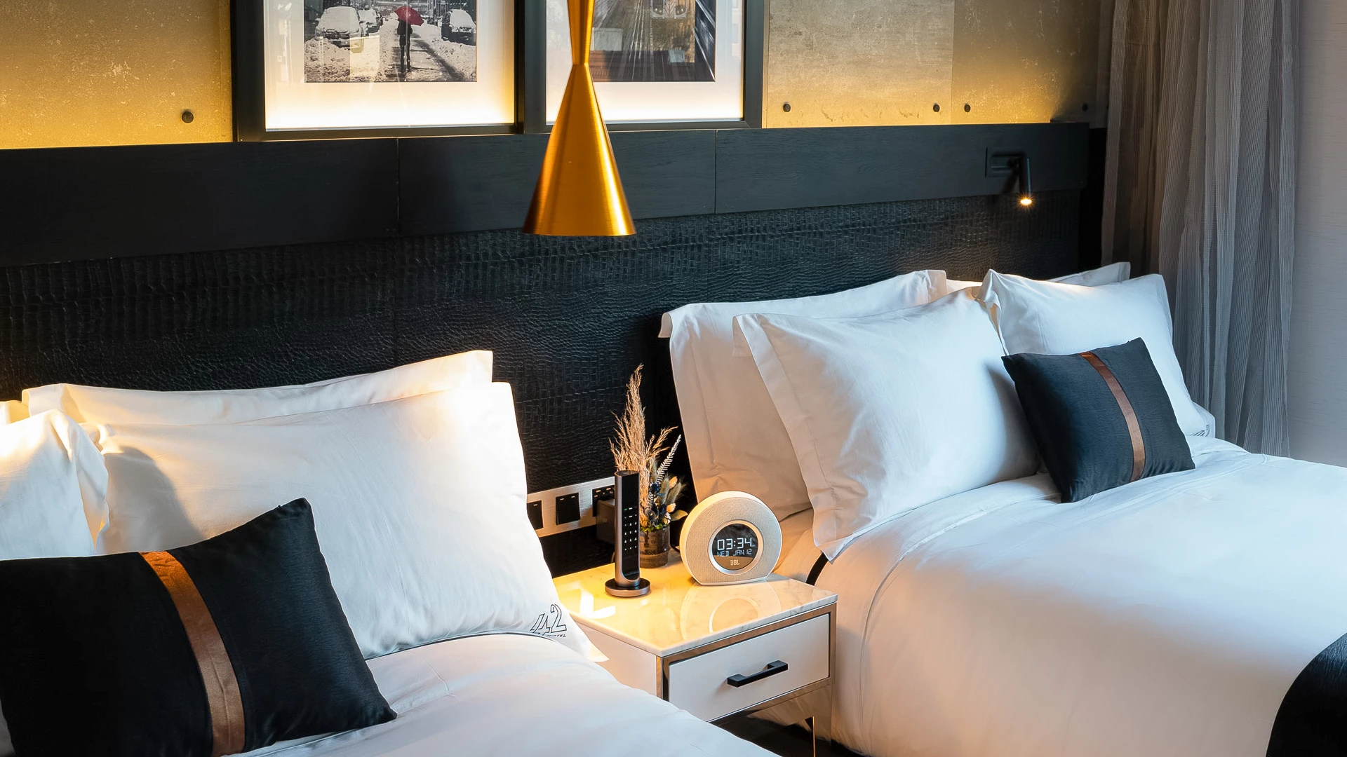 A hotel room with two beds, a black headboard, and a gold lamp.
