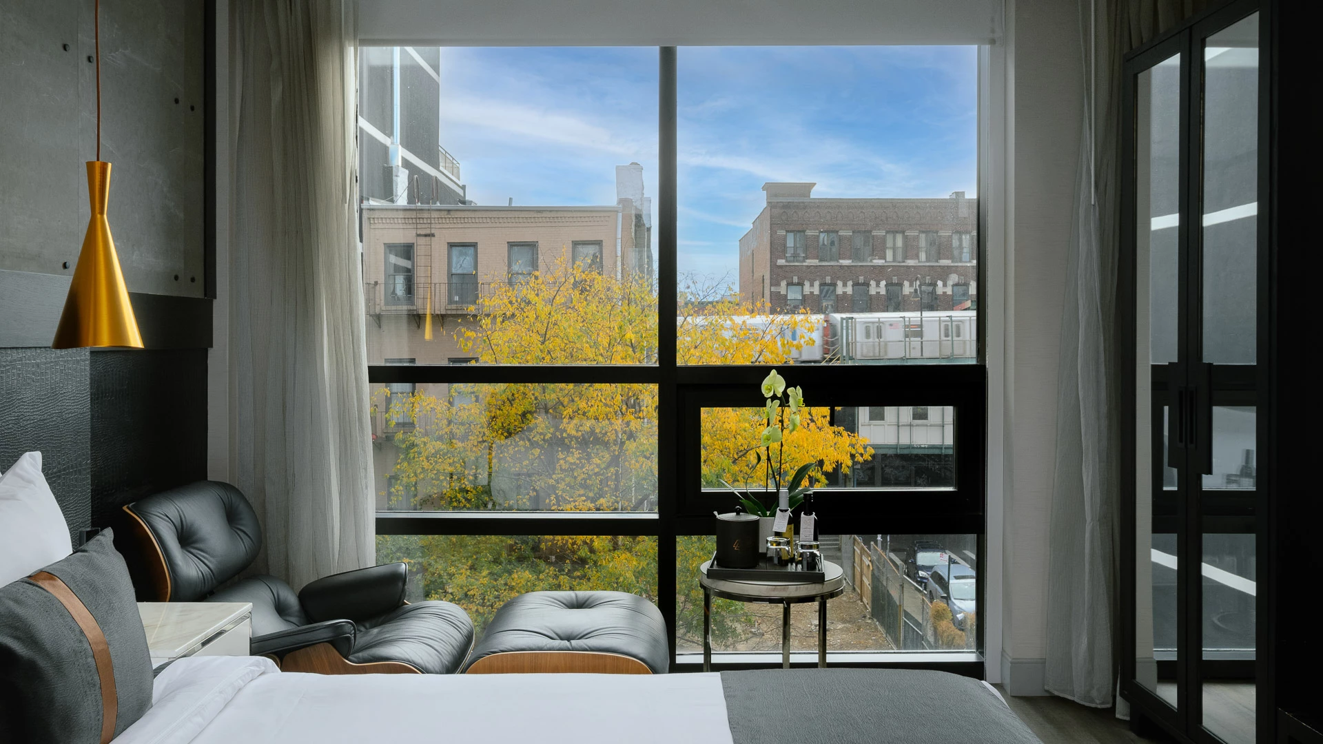 A hotel room with a large window, bed, chair, and table.