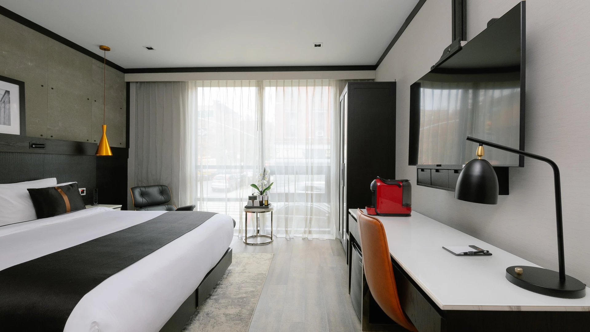 A hotel room with a bed, desk, TV, and window