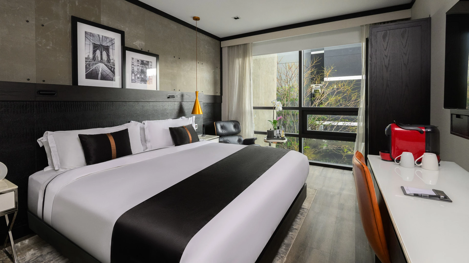 A modern hotel room with a large bed, desk, chair, and window.