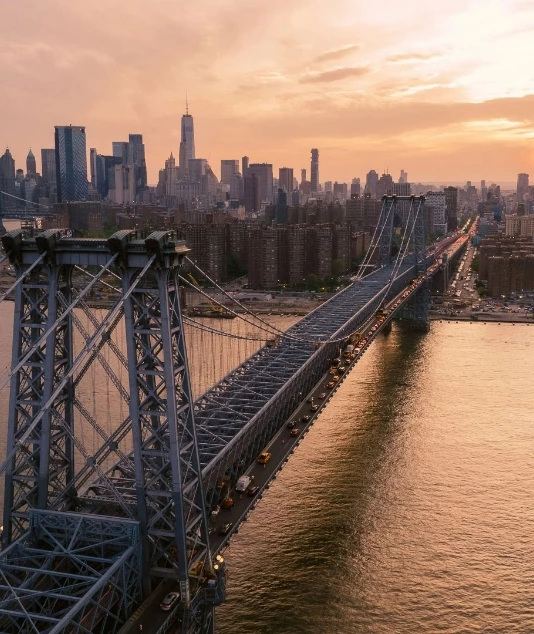 Aerial view of a bridge over a body of water with a city skyline in the background at sunset.