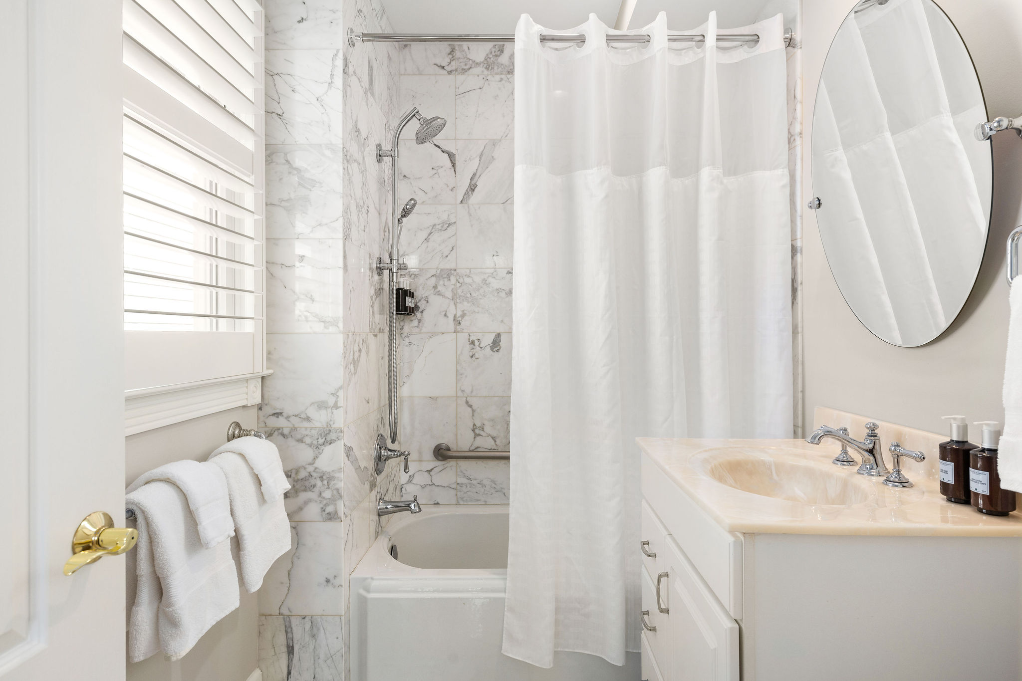 A clean and well-lit bathroom with marble tiles, a white sink, and a shower with a curtain.