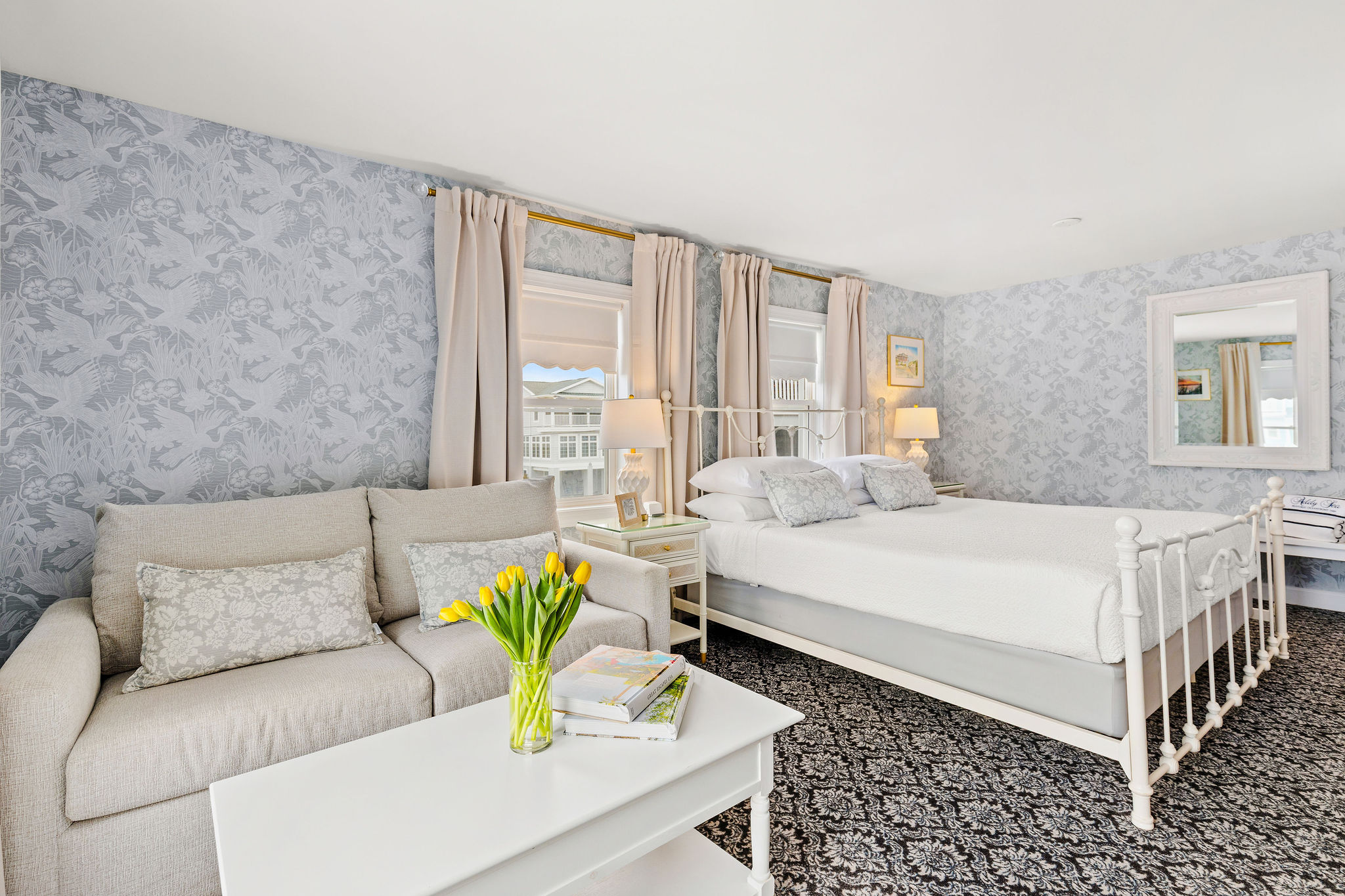 A wide view of a guest room with a sofa, coffee table, bed, window, and mirror.