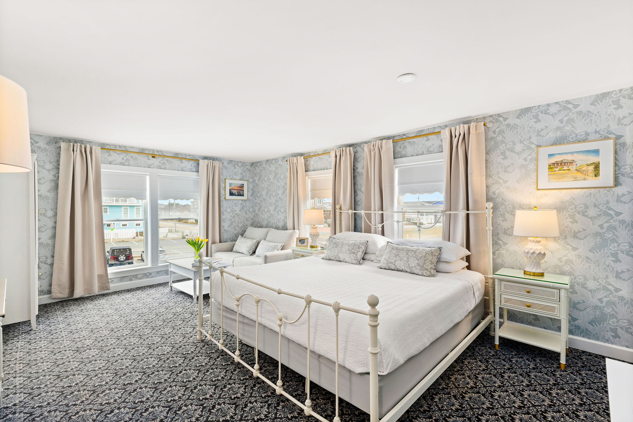 A wide view of a guest room with a white bed, gray walls, and carpeted floor.