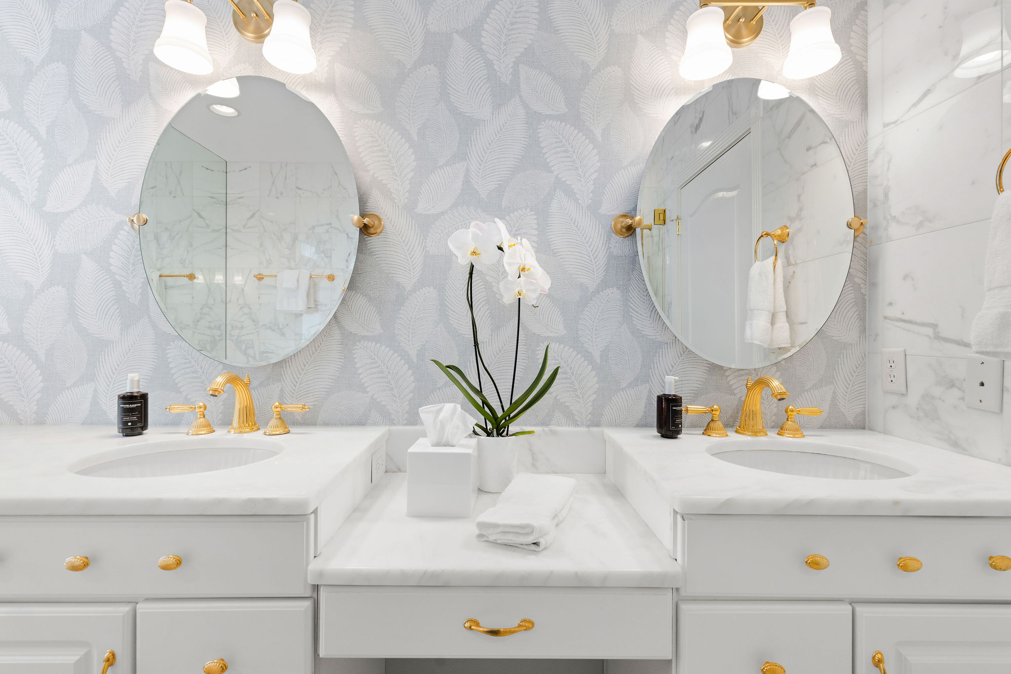 A clean and elegant bathroom vanity with two sinks, gold fixtures, and a decorative orchid.