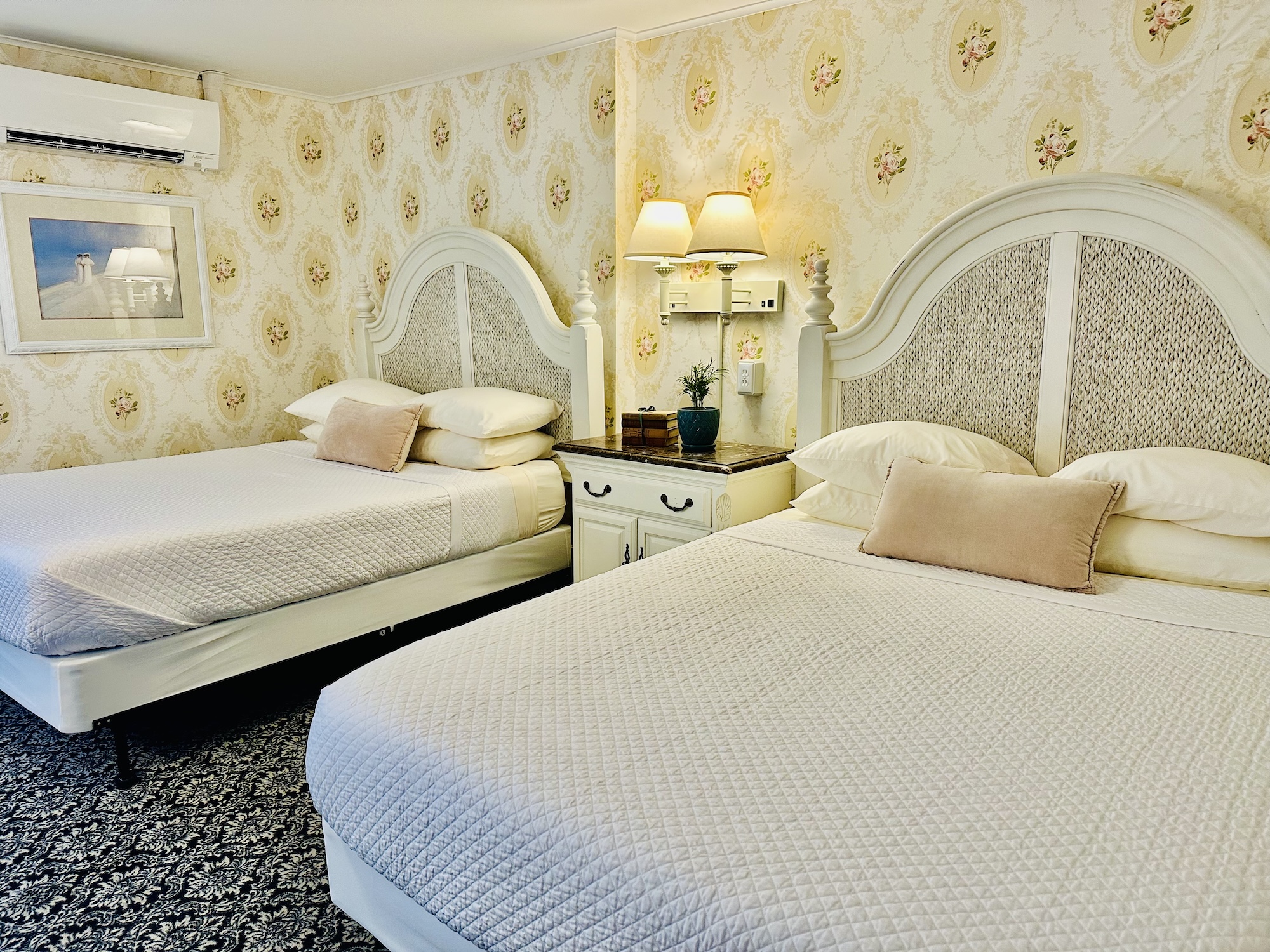 A hotel room with two beds, floral wallpaper, and a nightstand between them.