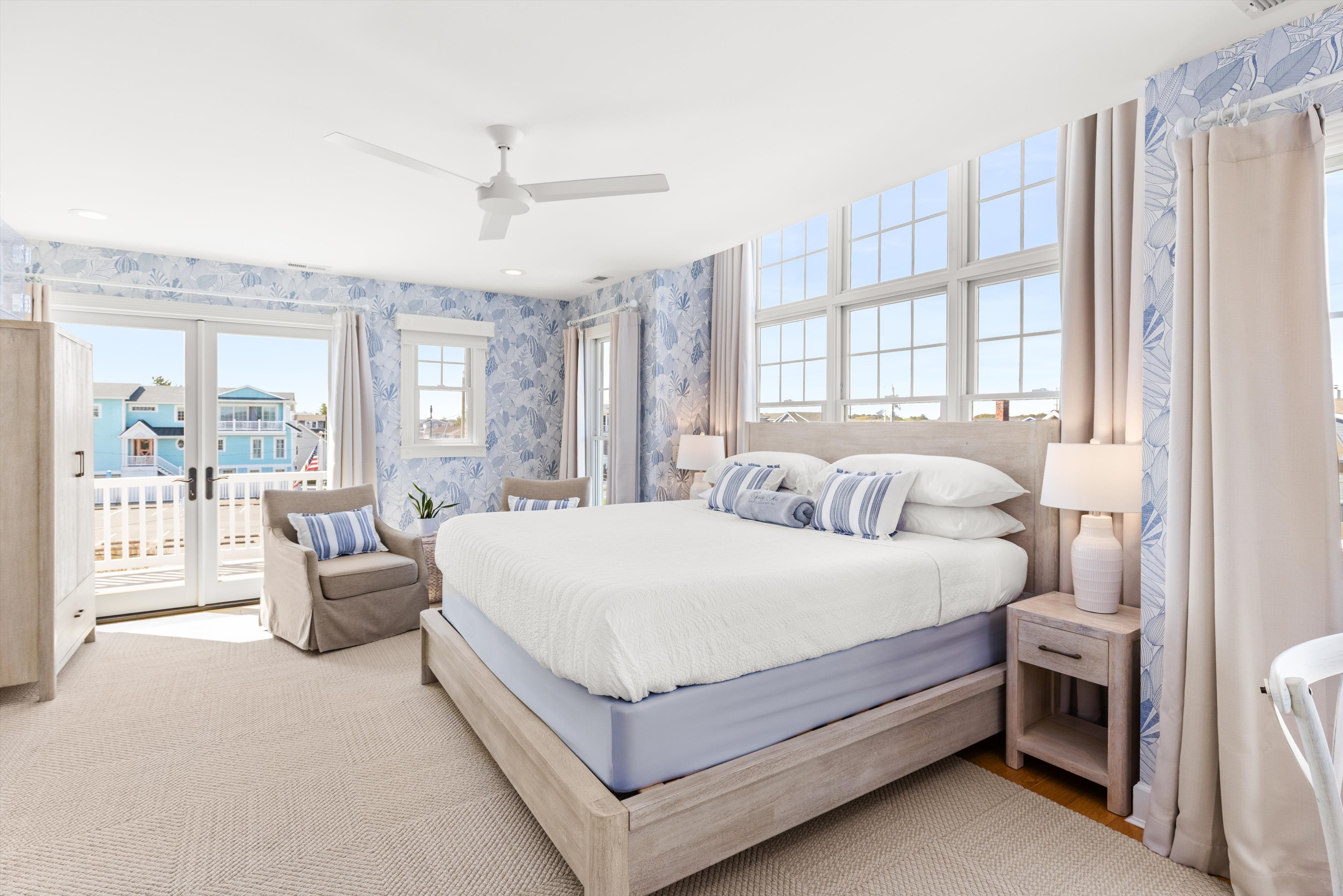 A wide-angle view of a guest room with a large bed, dresser, armchair, and balcony door.