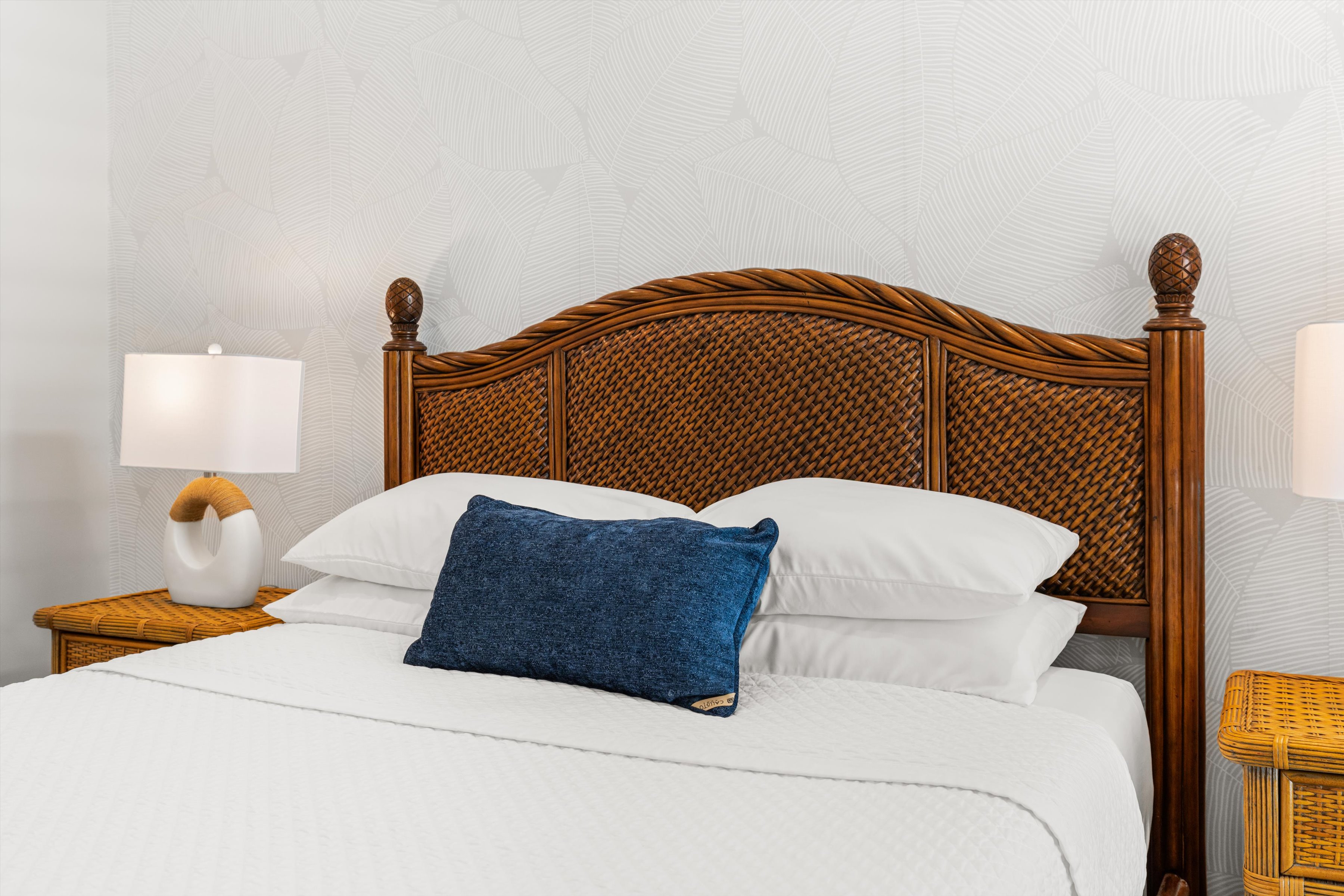 A neatly made bed with a wicker headboard, white bedding, and a blue accent pillow.