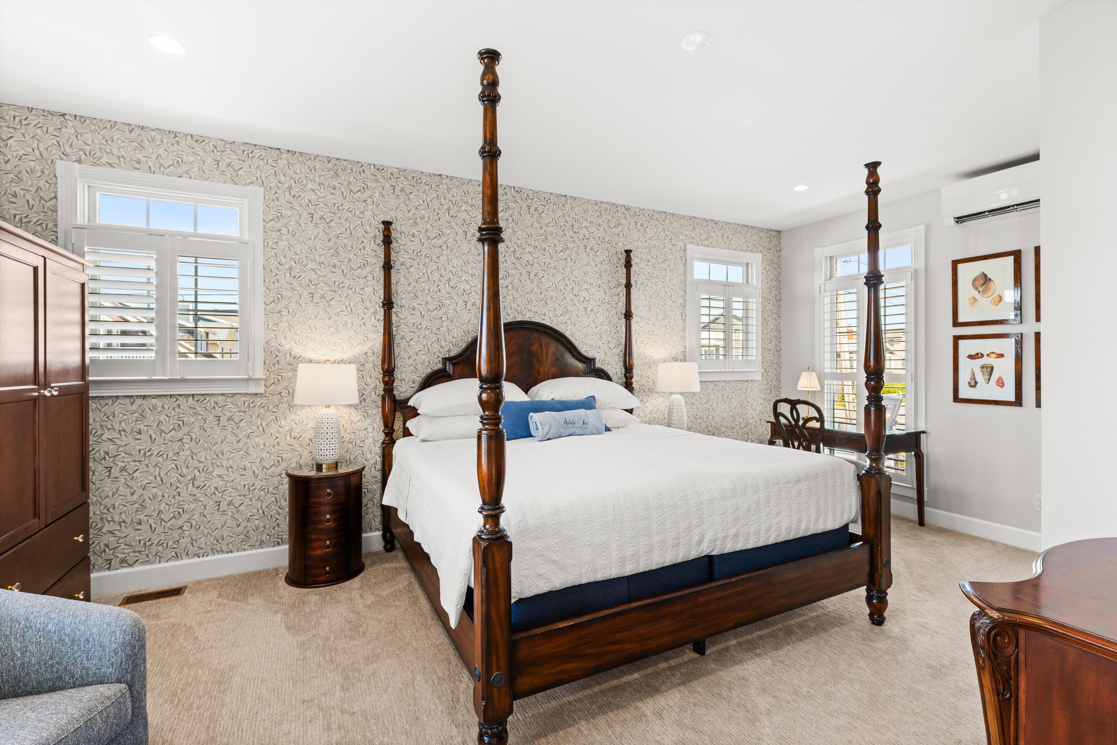 A wide view of a guest room with a four-poster bed, patterned wallpaper, and wood furniture.