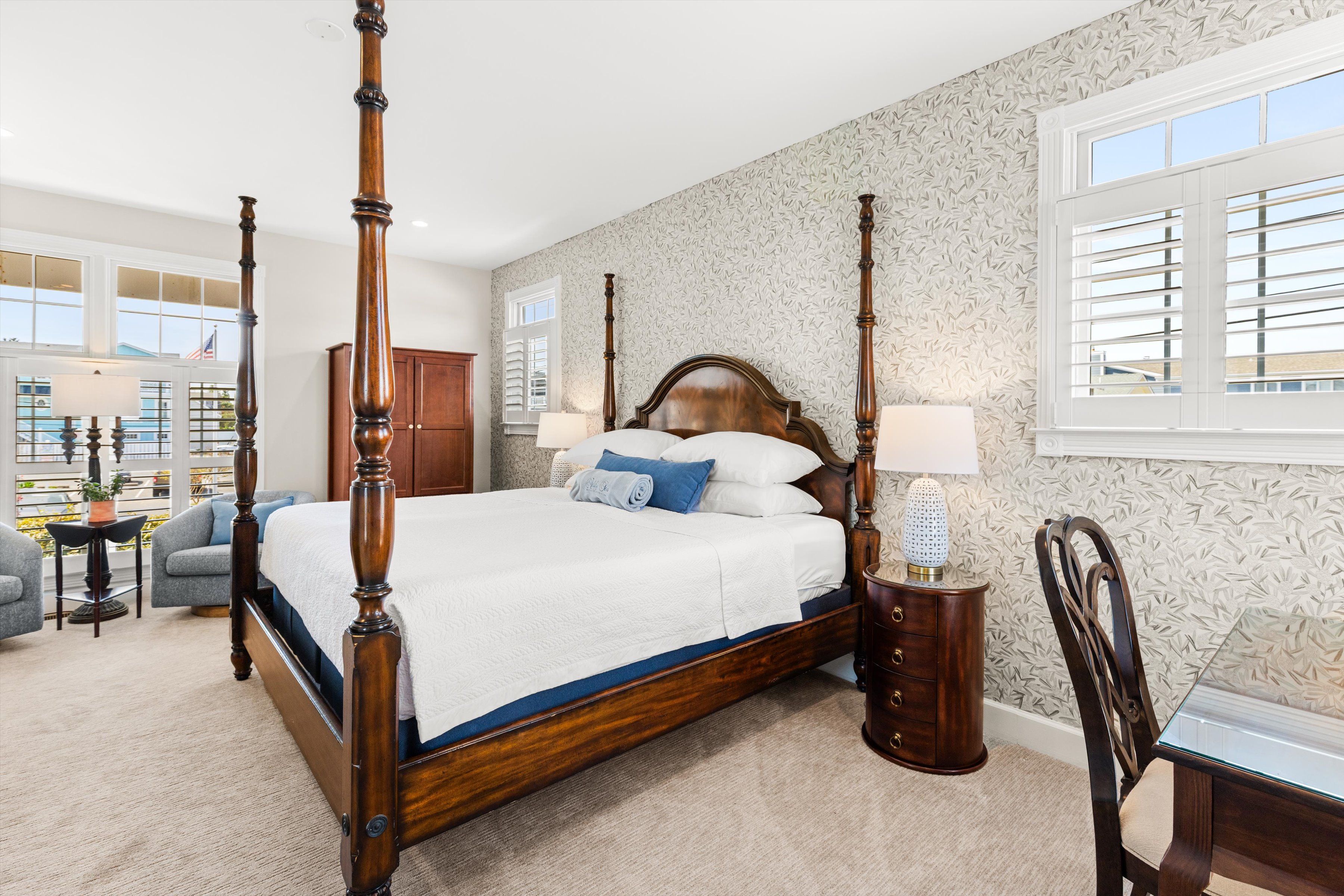 A wide view of a guest room with a four-poster bed, desk, armchair, and window.
