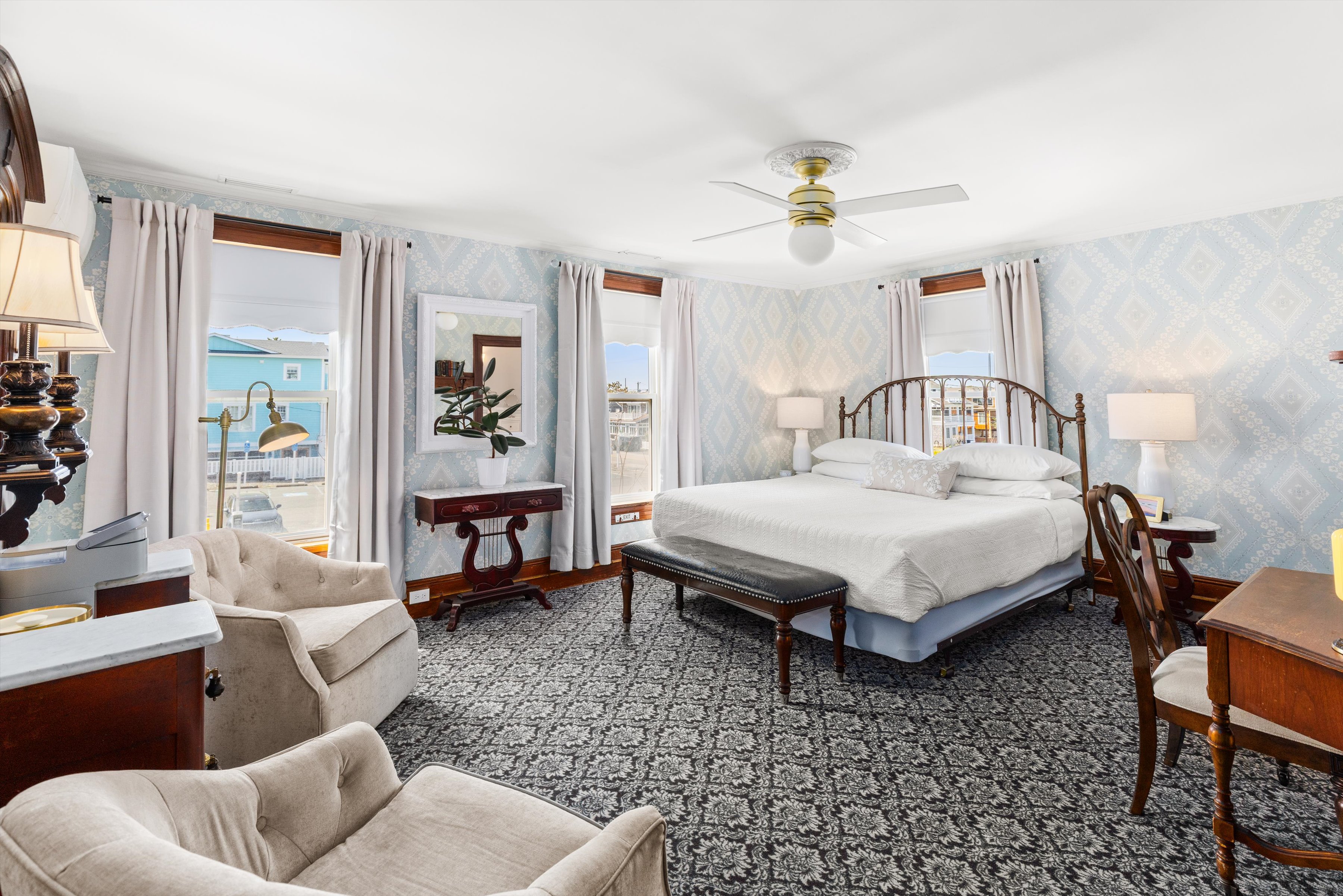 A wide view of a guest room with a bed, desk, chair, and window.