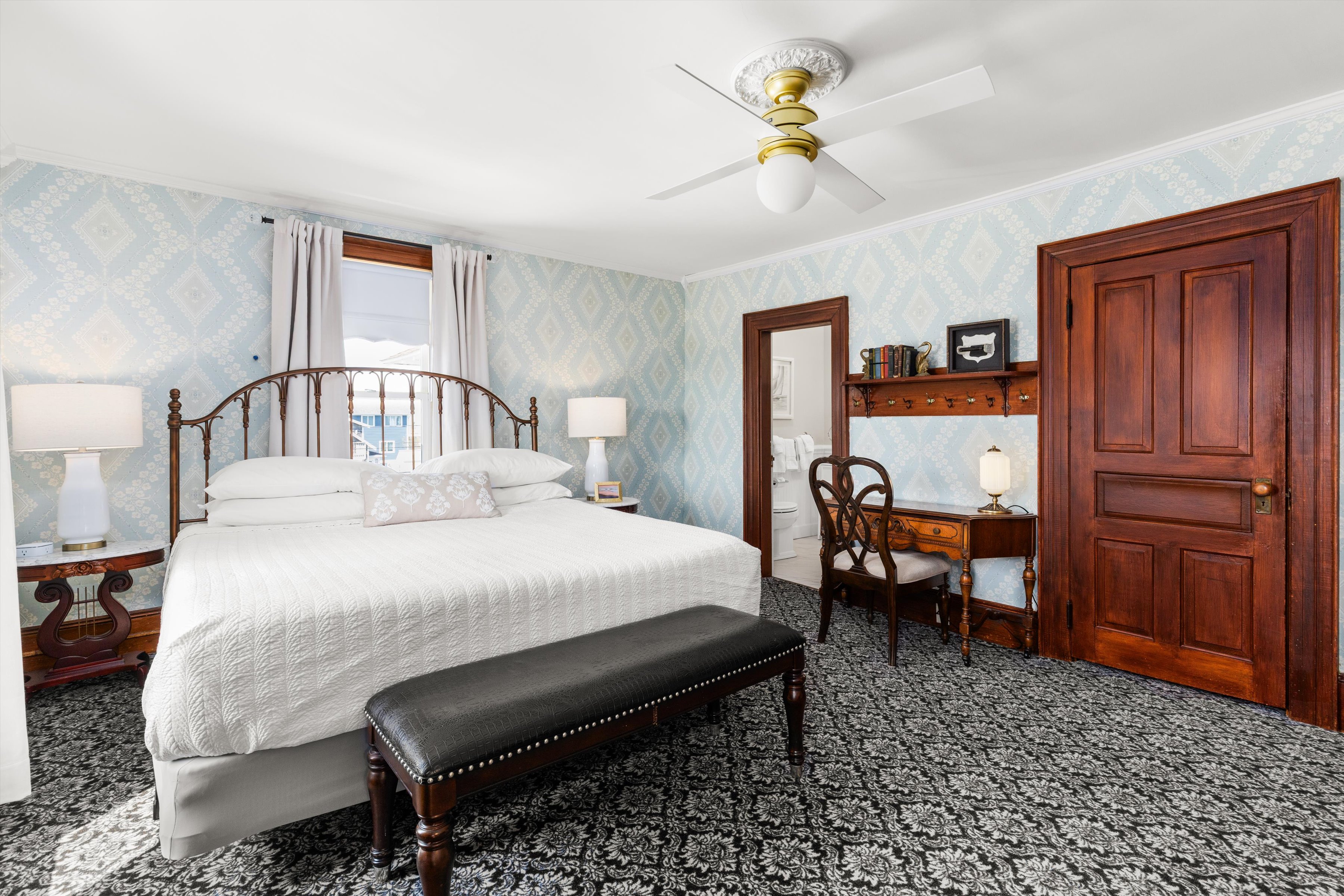 A wide view of a guest room with a large bed, desk area, and window.