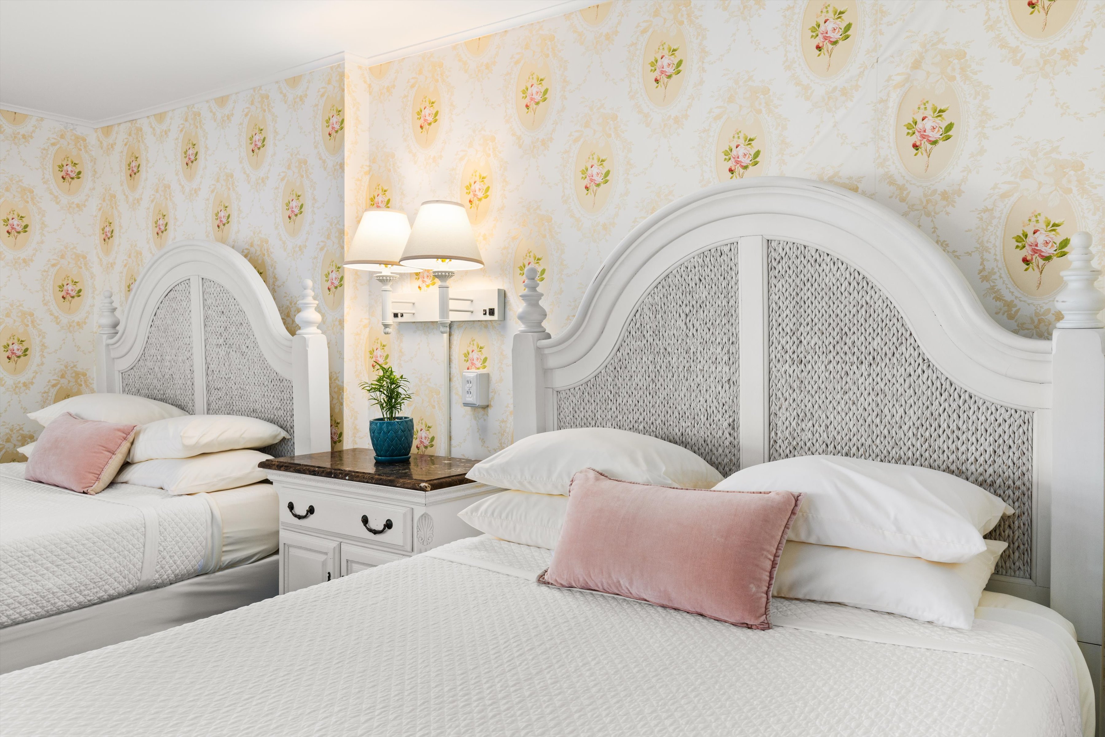 A neatly arranged hotel room with two beds, floral wallpaper, and pink accents.