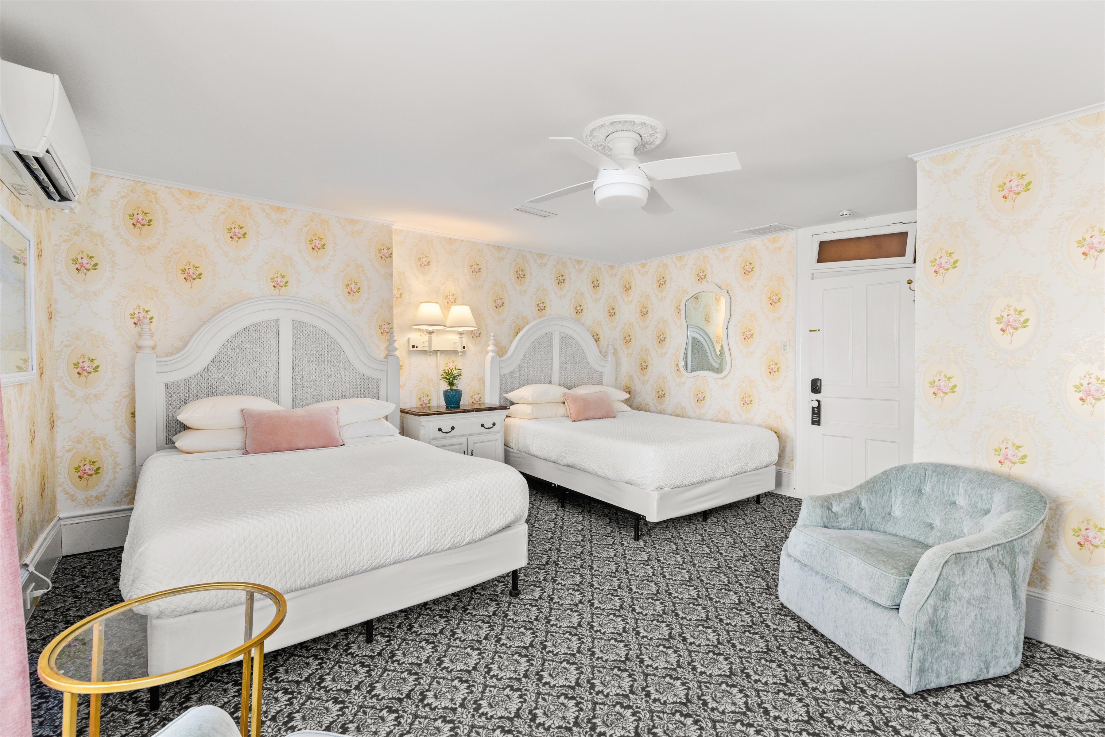 A wide view of a hotel room with two twin beds, floral wallpaper, and a patterned carpet.