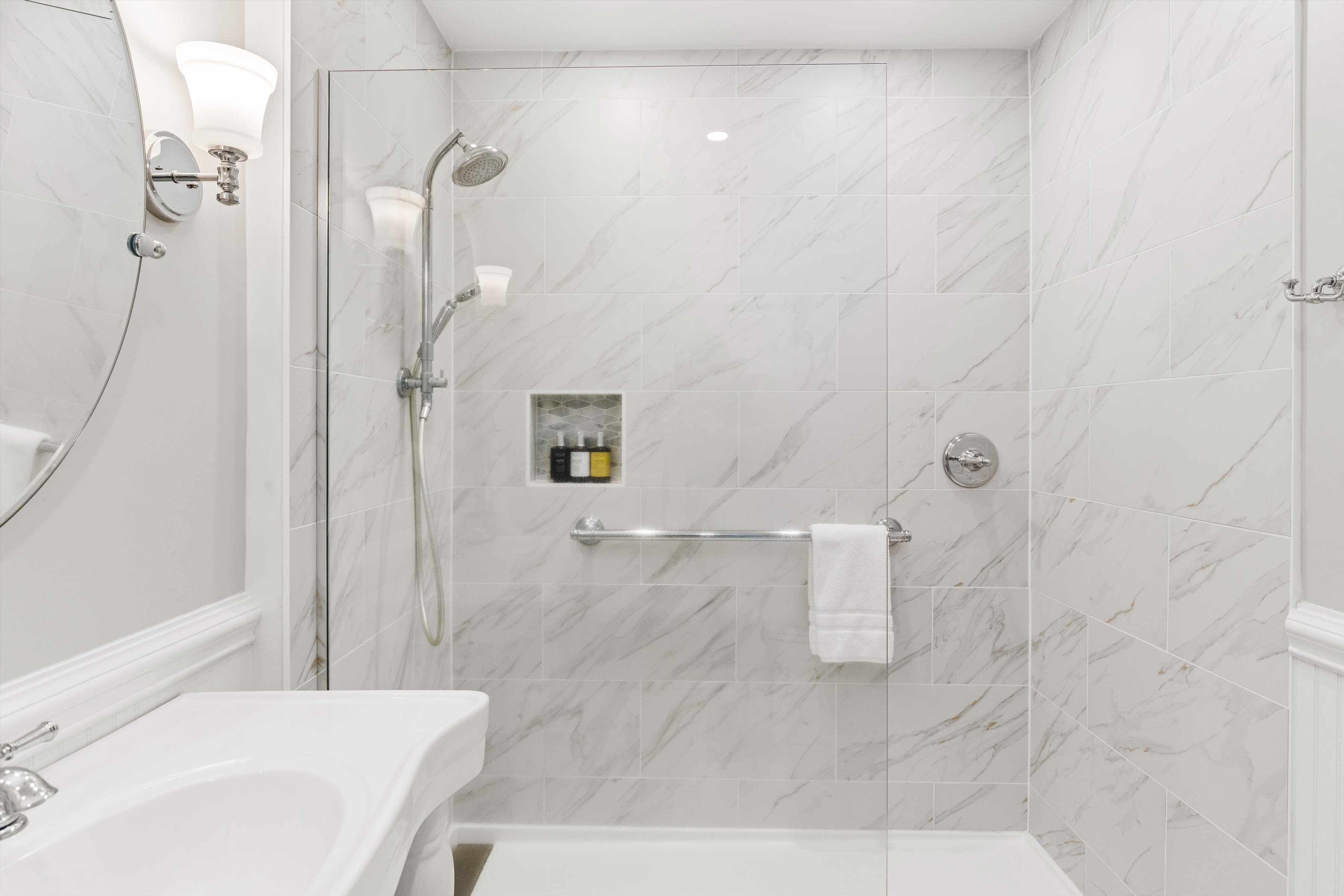 A clean and modern bathroom with a glass-enclosed shower and marble tiles.