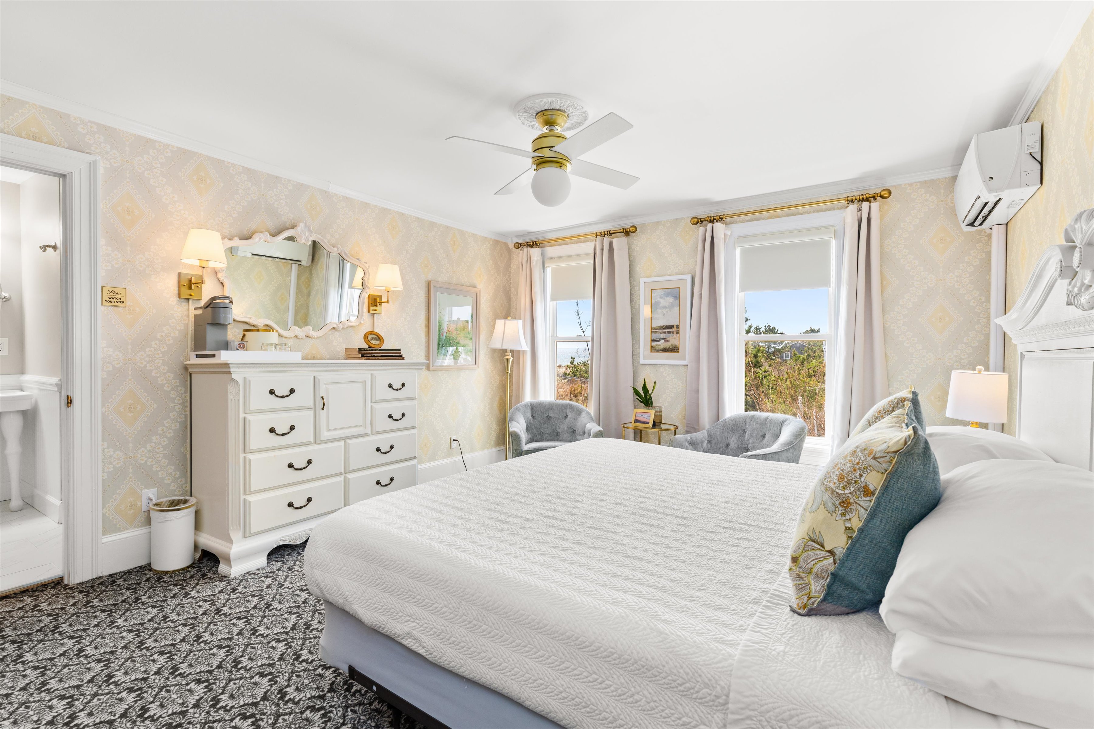 A wide view of a guest room with a large bed, dresser, and window