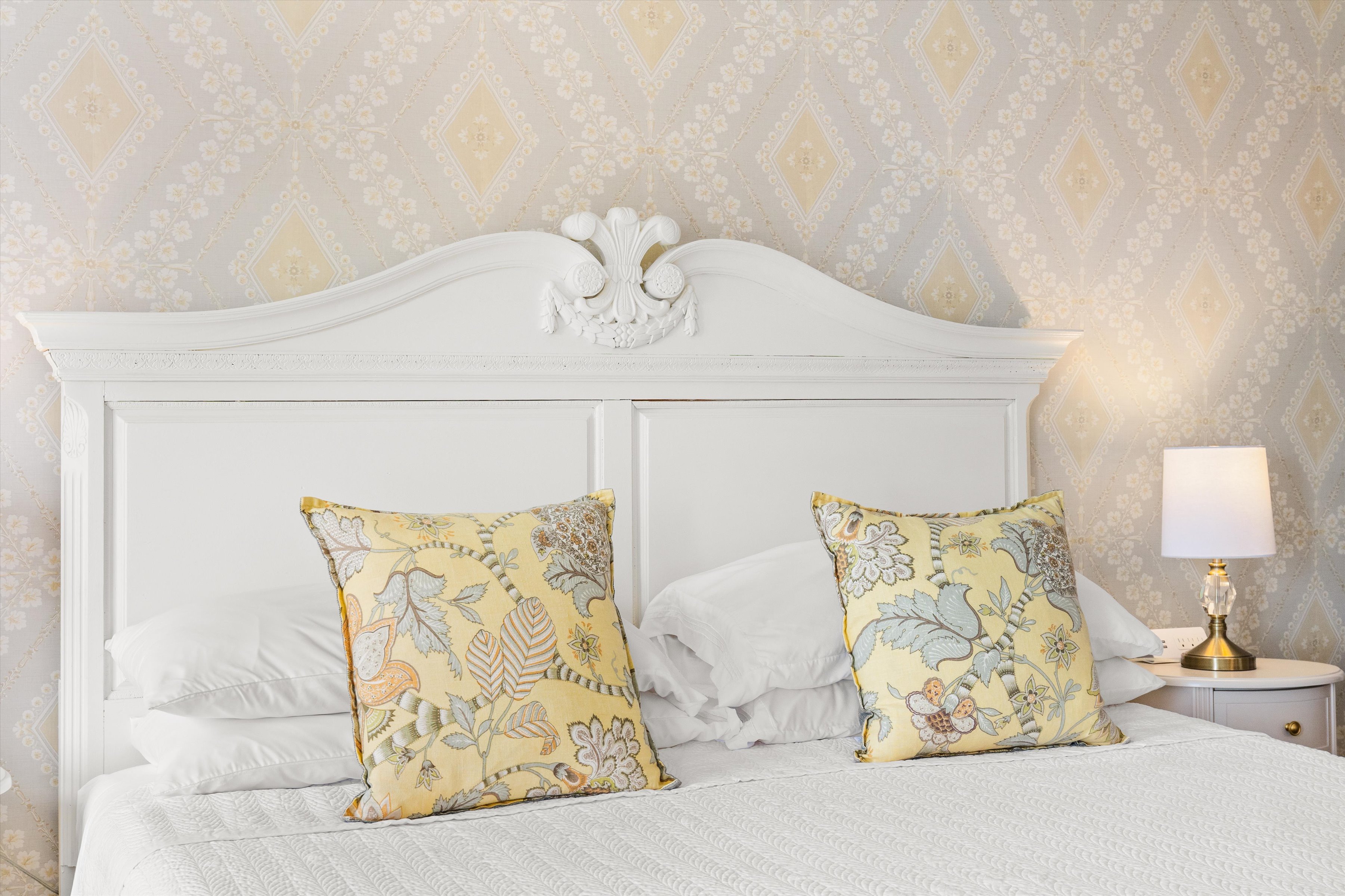 A neatly made bed with a white headboard and yellow floral pillows