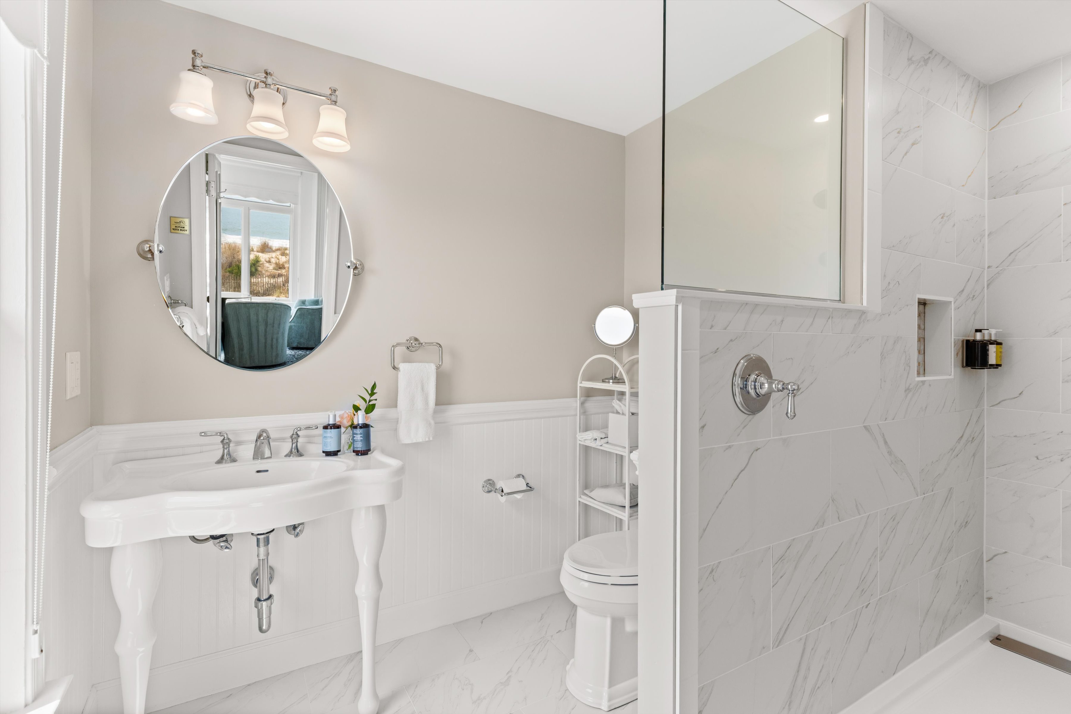 A clean and modern bathroom with a white sink, round mirror, shower, and toilet.