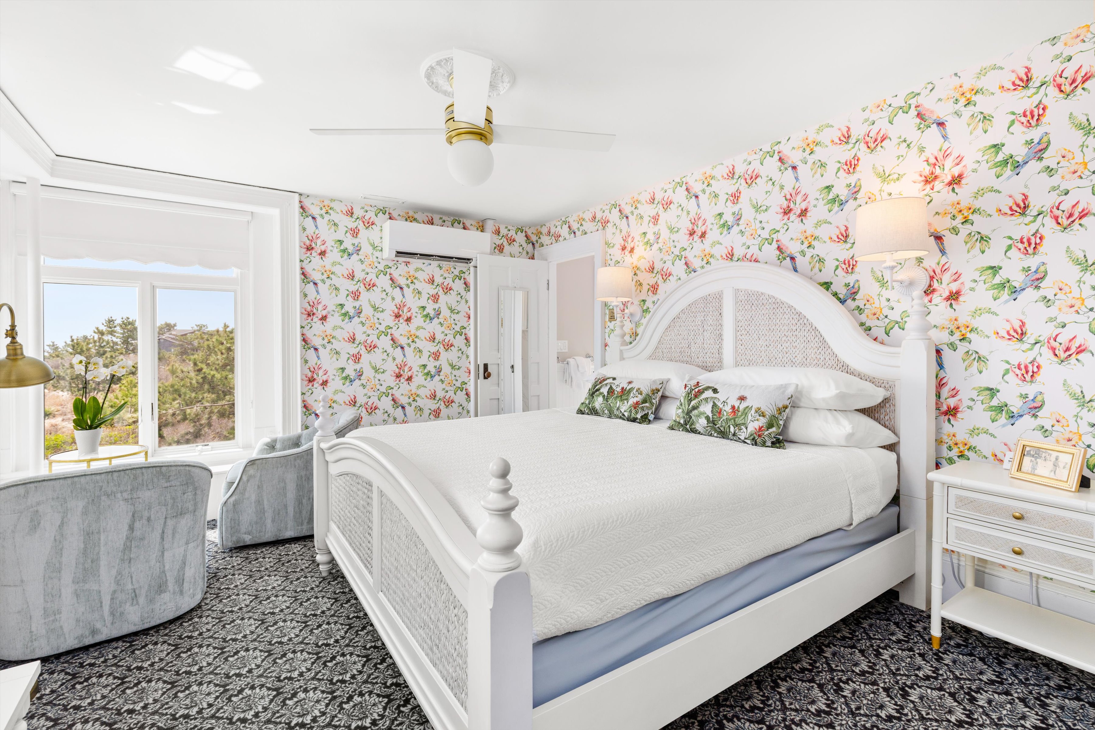 A bright and airy hotel room with a large bed, floral wallpaper, and a window with a view.