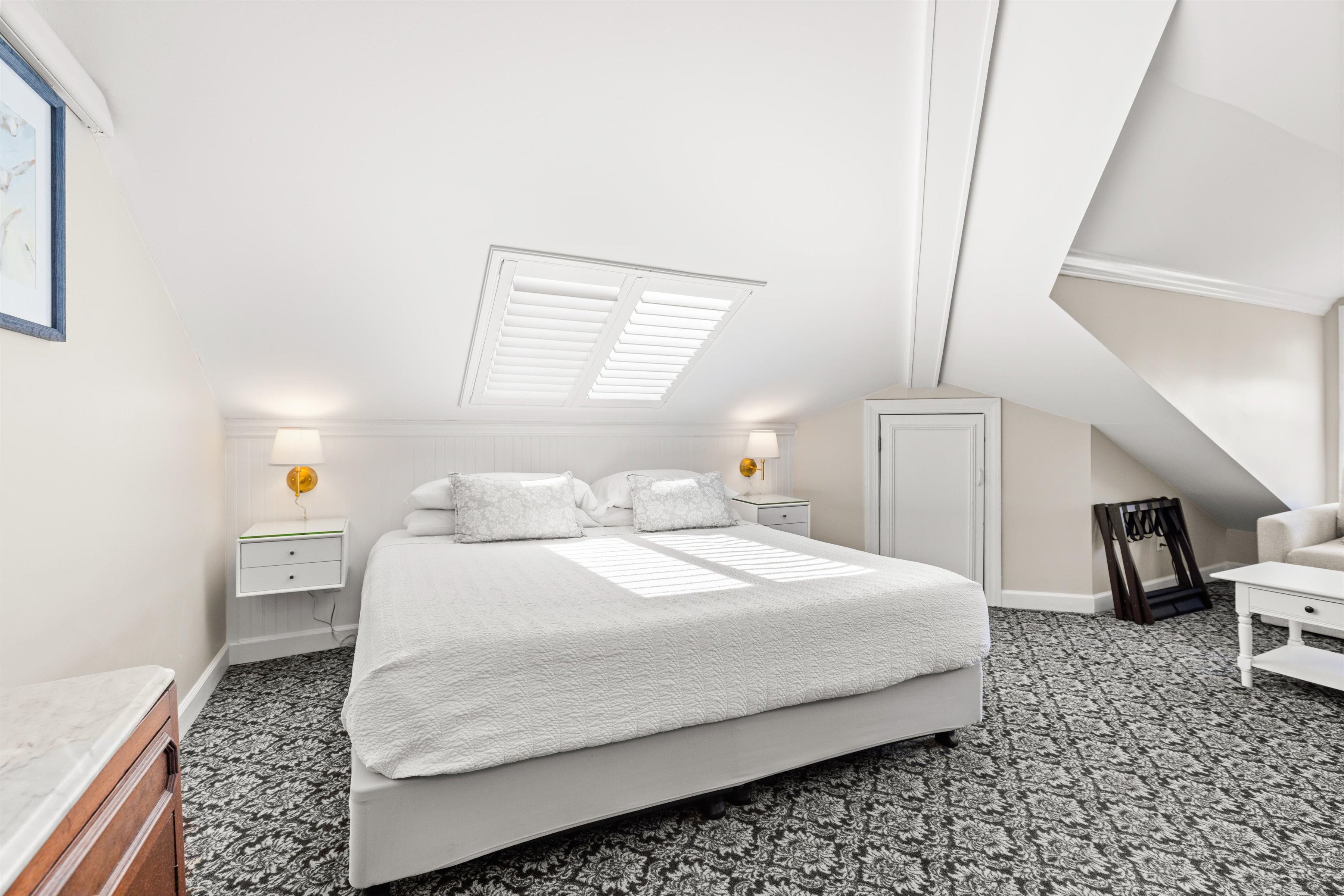 A wide view of a guest room with a bed, nightstands, and a skylight.