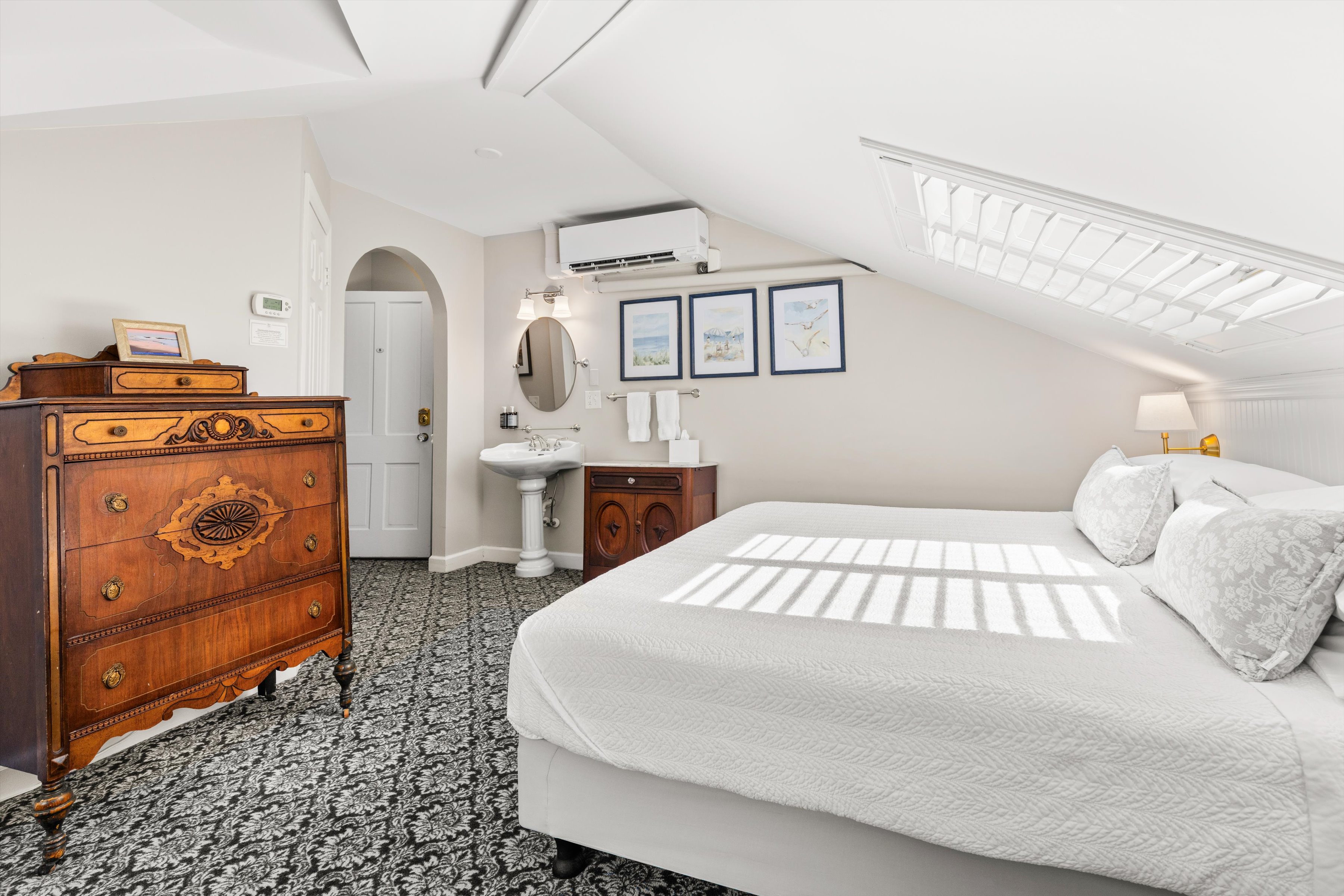 A wide view of a cozy bedroom with a large bed, wooden dresser, and small sink area.
