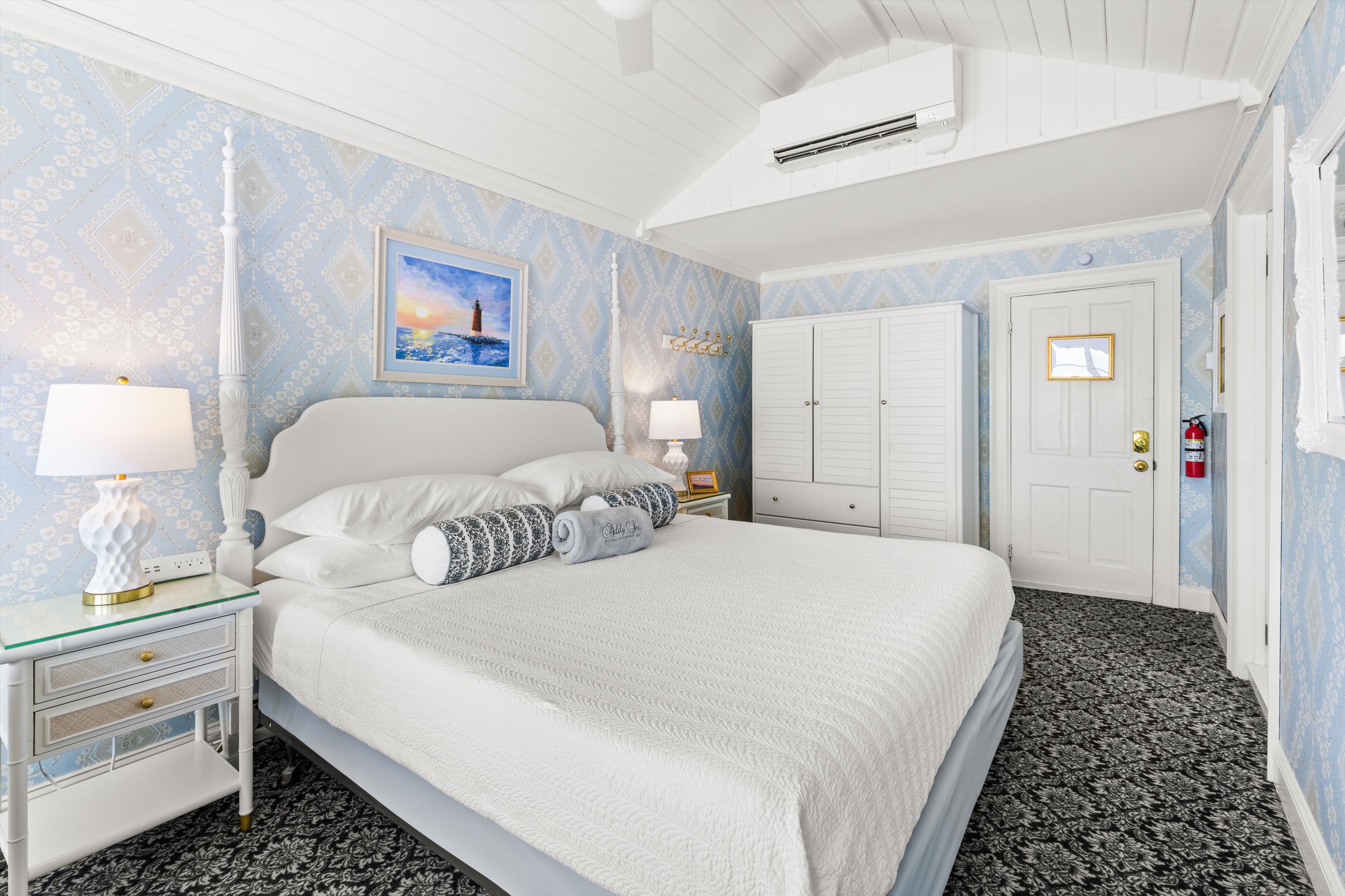 A clean and cozy hotel room with a white bed, blue wallpaper, and a large window.